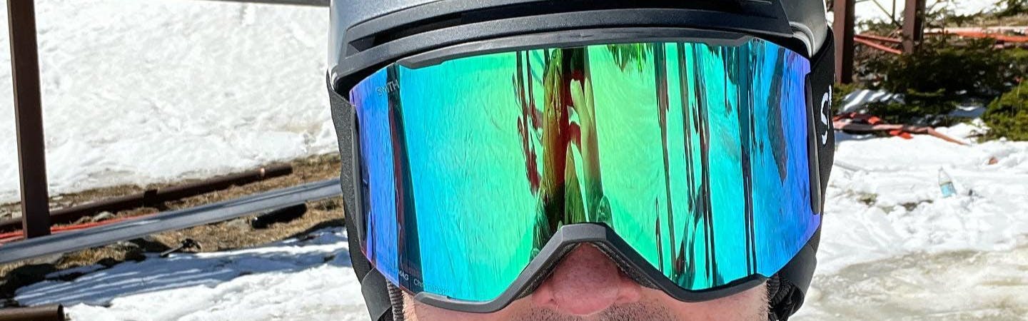 Close up of a skier wearing the ChromaPop Mirror Green on the Smith Squad MAG Goggles. There is snow in the background. 