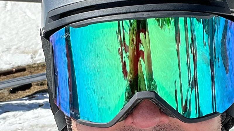 Close up of a skier wearing the ChromaPop Mirror Green on the Smith Squad MAG Goggles. There is snow in the background. 