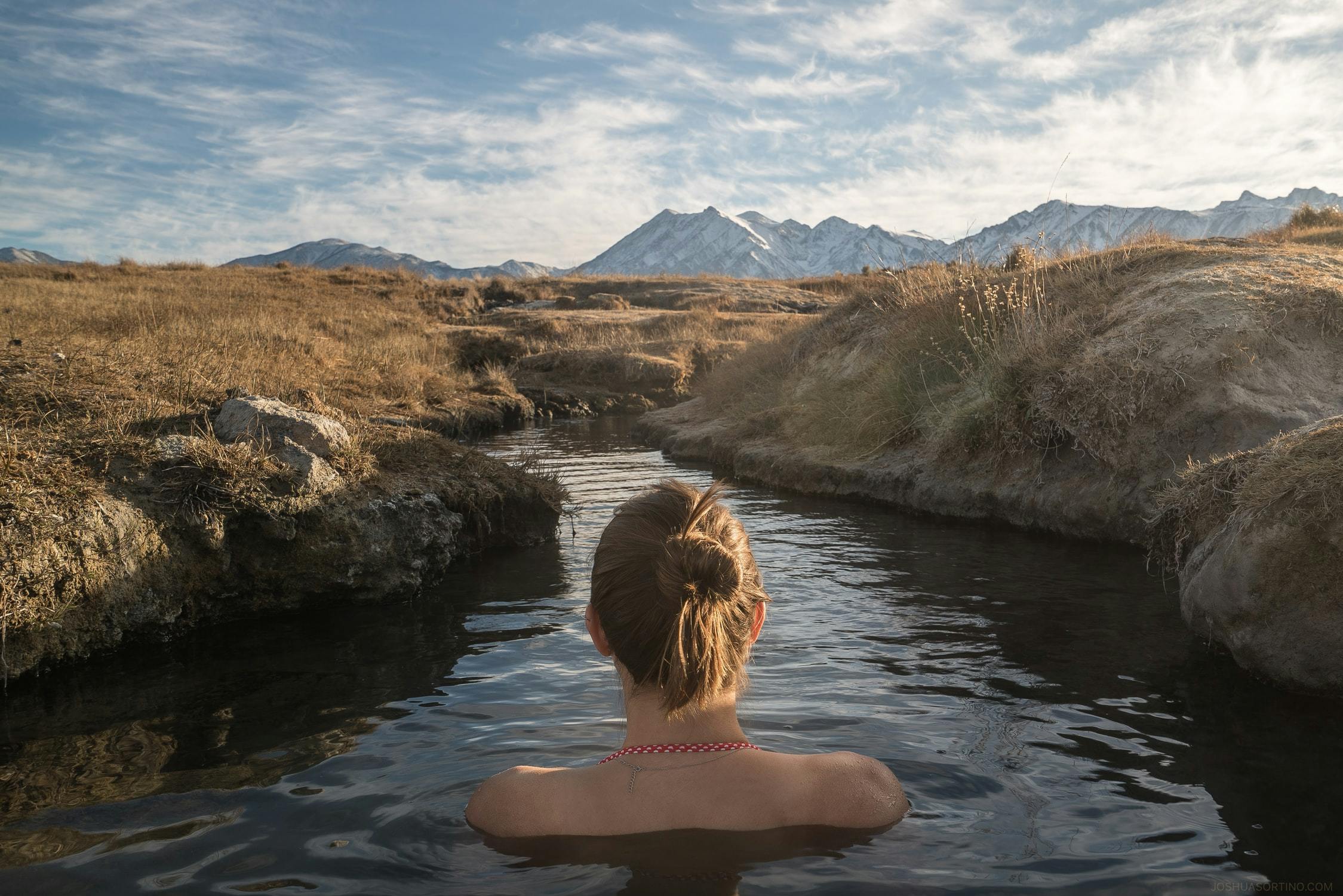 A woman in a hot springs looking out at the mountains in the distance