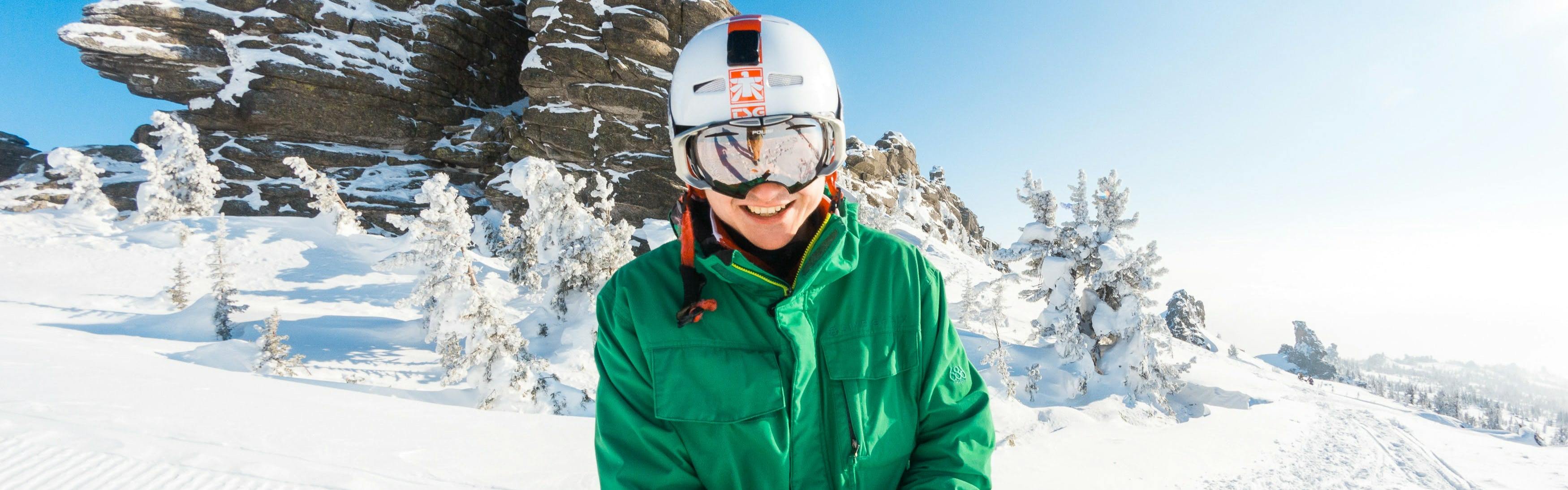 A skier wearing a helmet and goggles. There is a snowy trail behind him. 