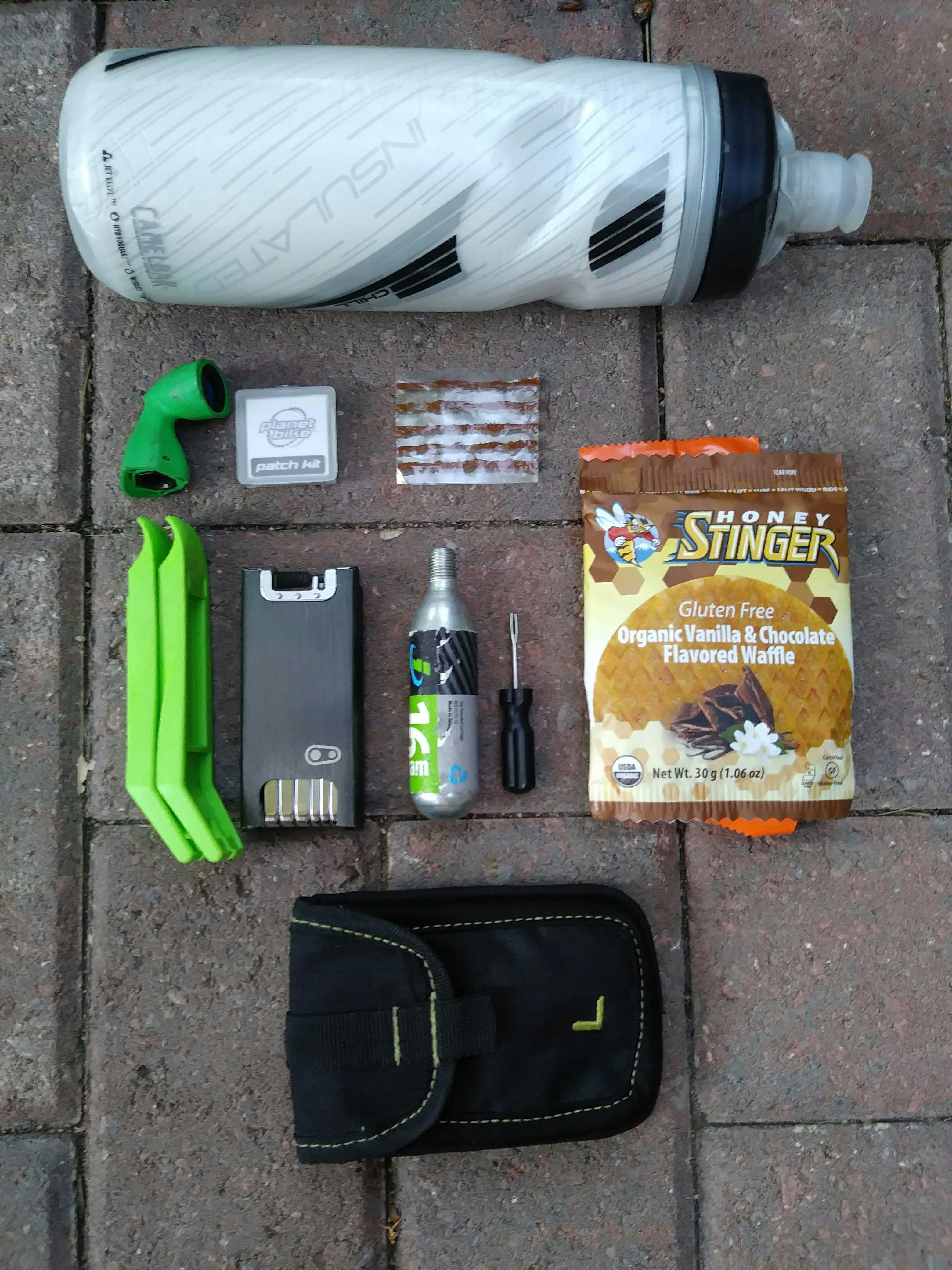 An array of bike tools, a water bottle, and a snack on a brick ground