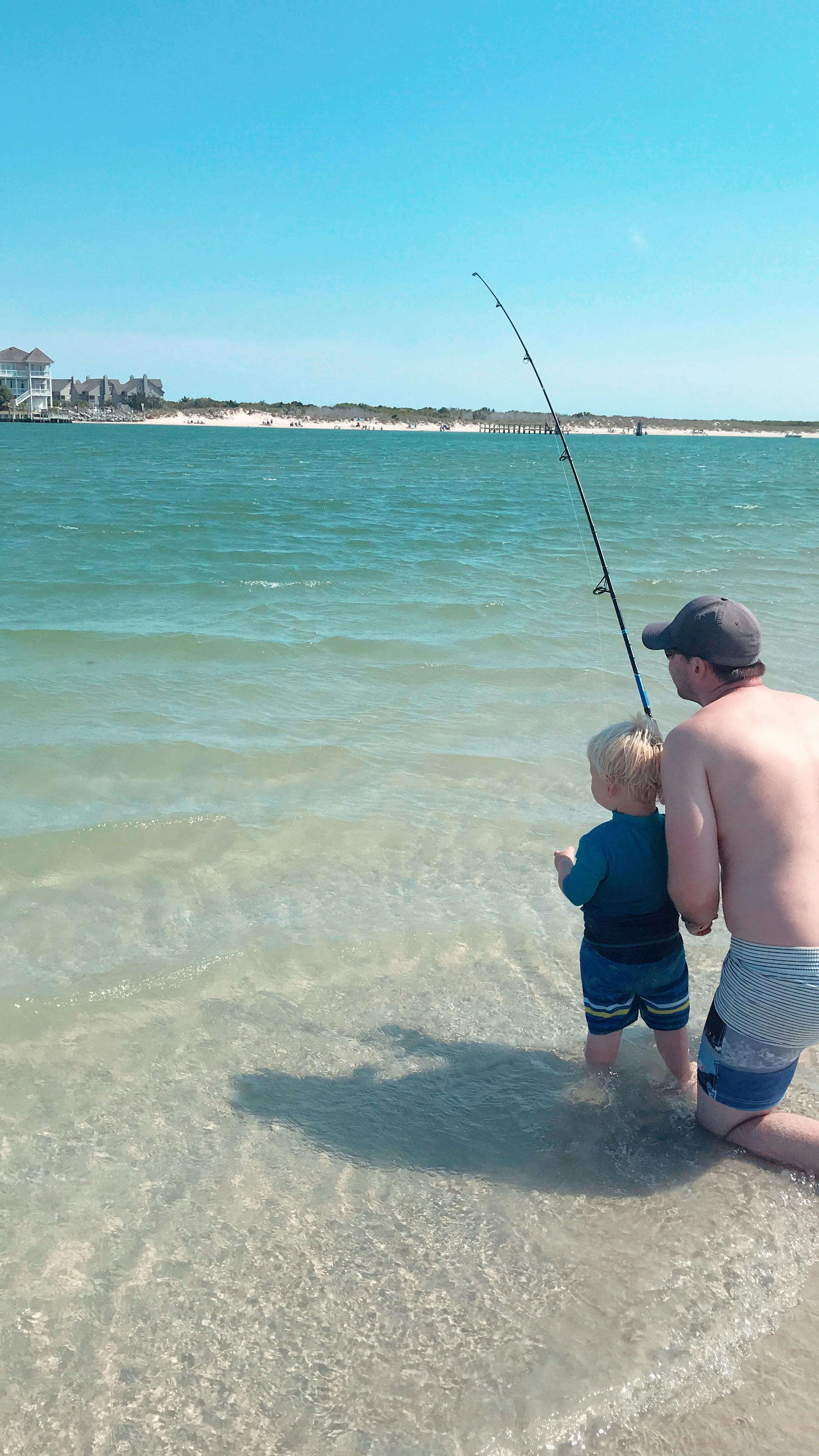 A father and child fish in a clear water bay.