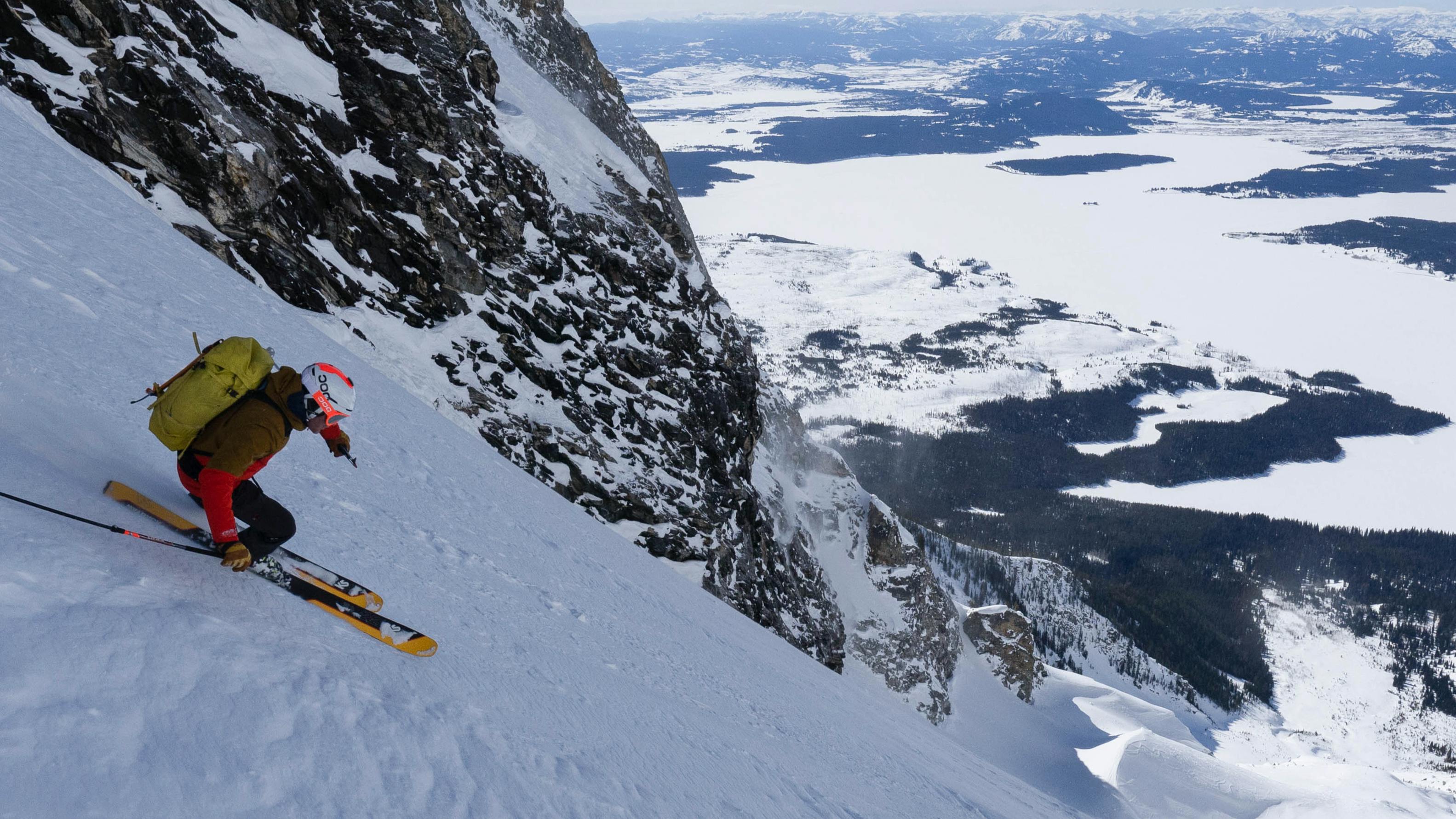 A skier turning down a steep, snowy mountain. There are snowy mountains in the background. 