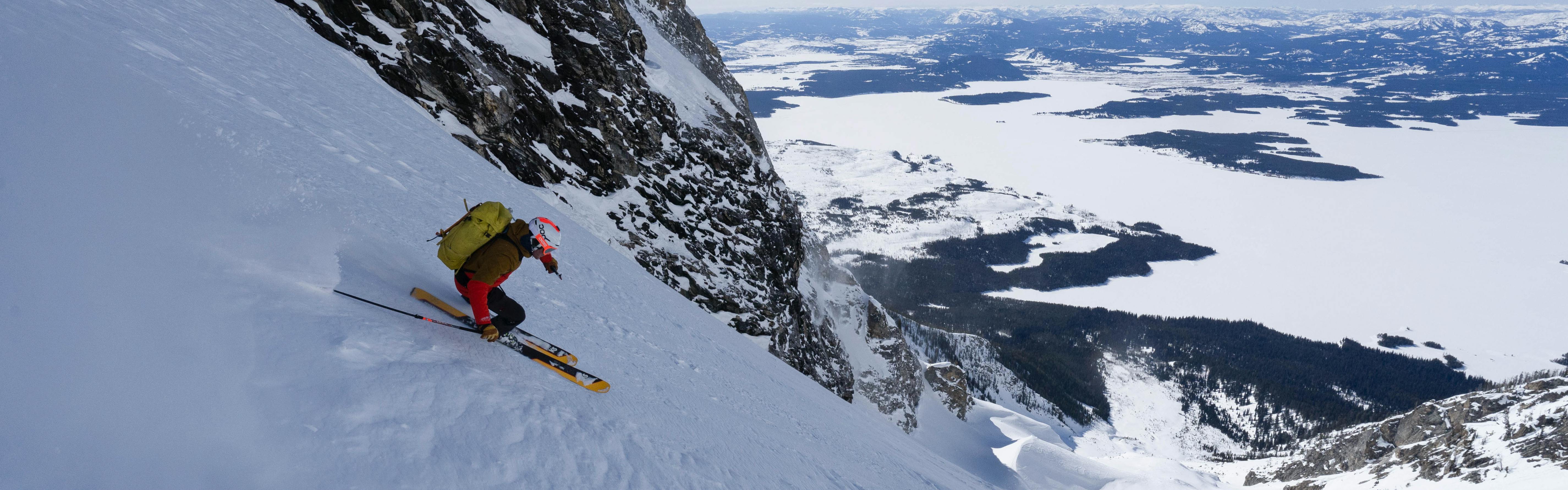A skier turning down a steep, snowy mountain. There are snowy mountains in the background. 