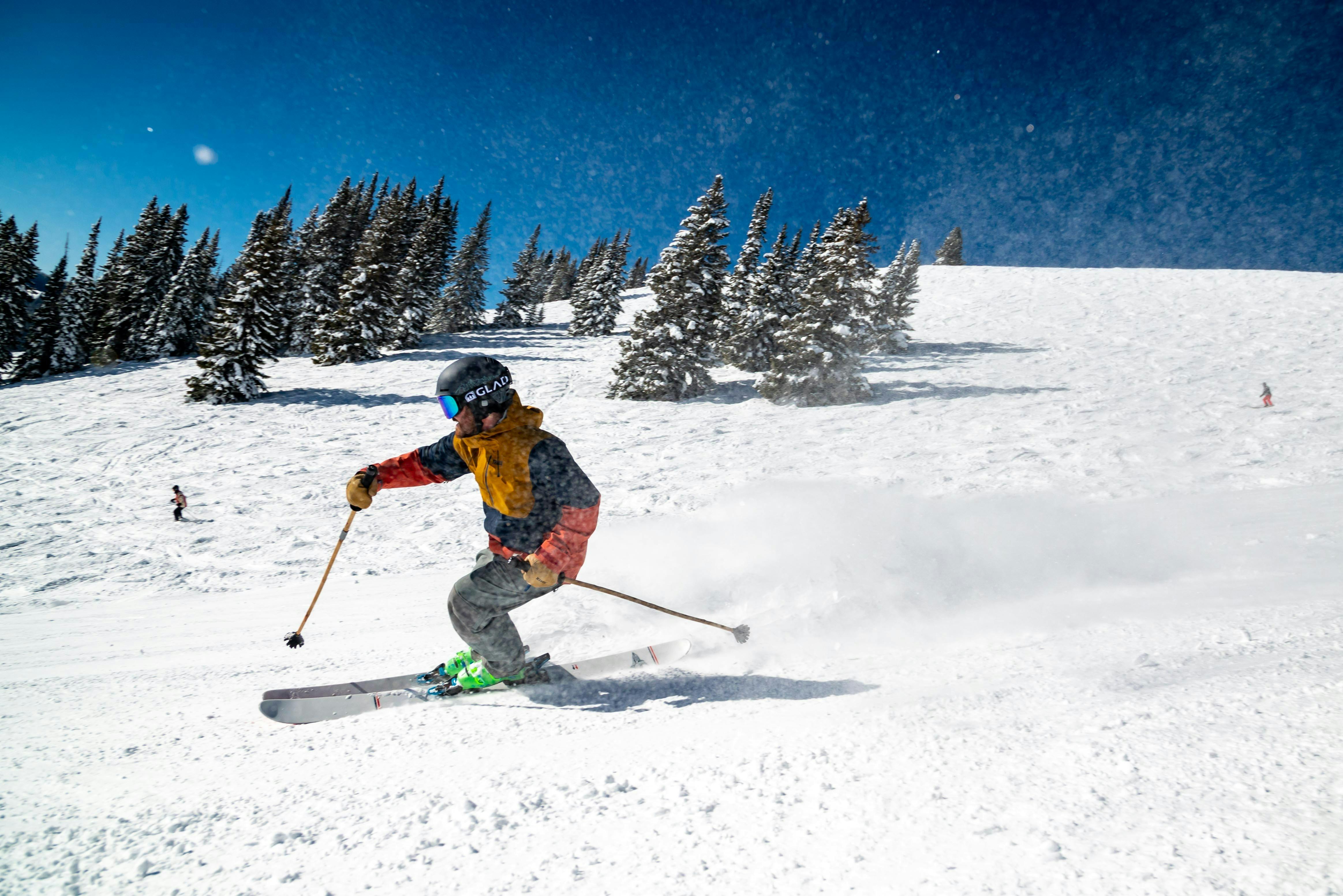 A skier in an orange jacket turns down a ski run. 