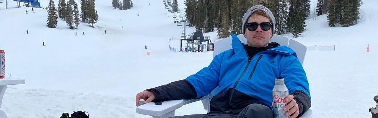 A man sitting in a lawn chair at a ski resort wearing the North Face Men's Sickline Insulated Jacket.