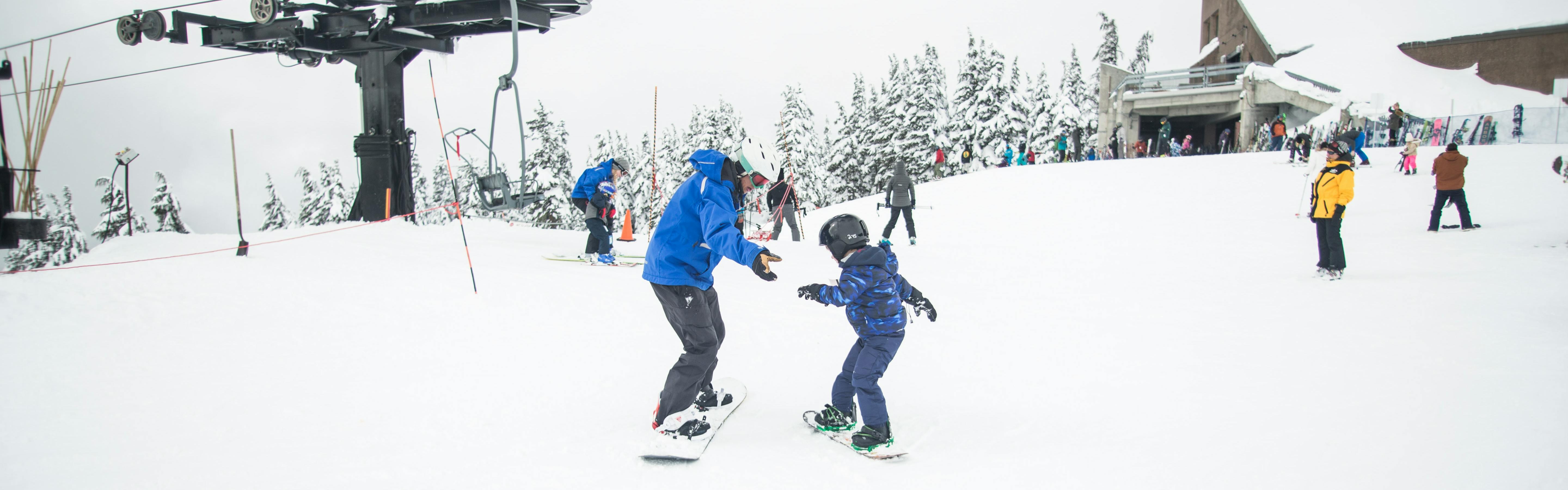 A child learns how to snowboard across from an instructor. 