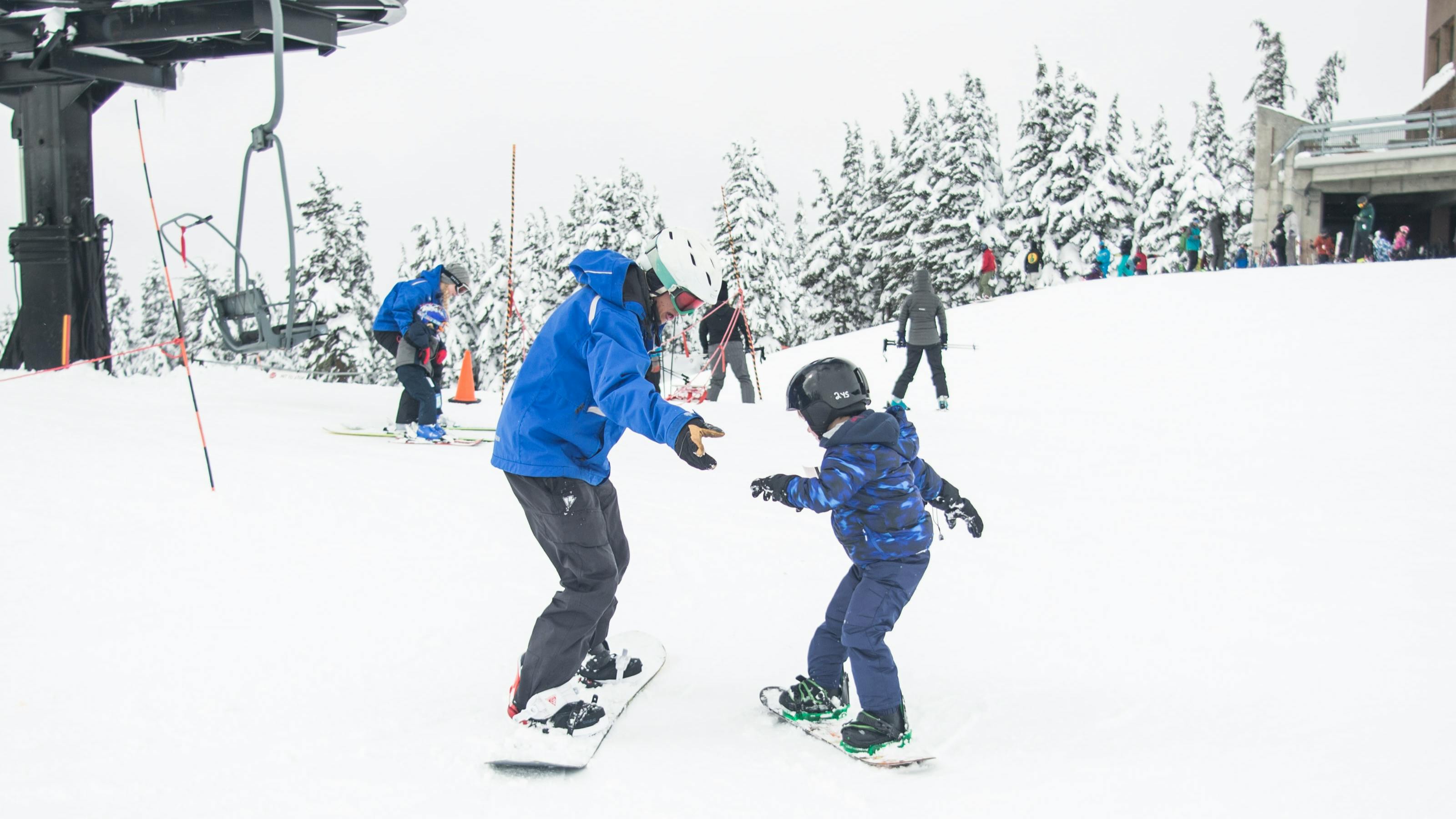 A child learns how to snowboard across from an instructor. 