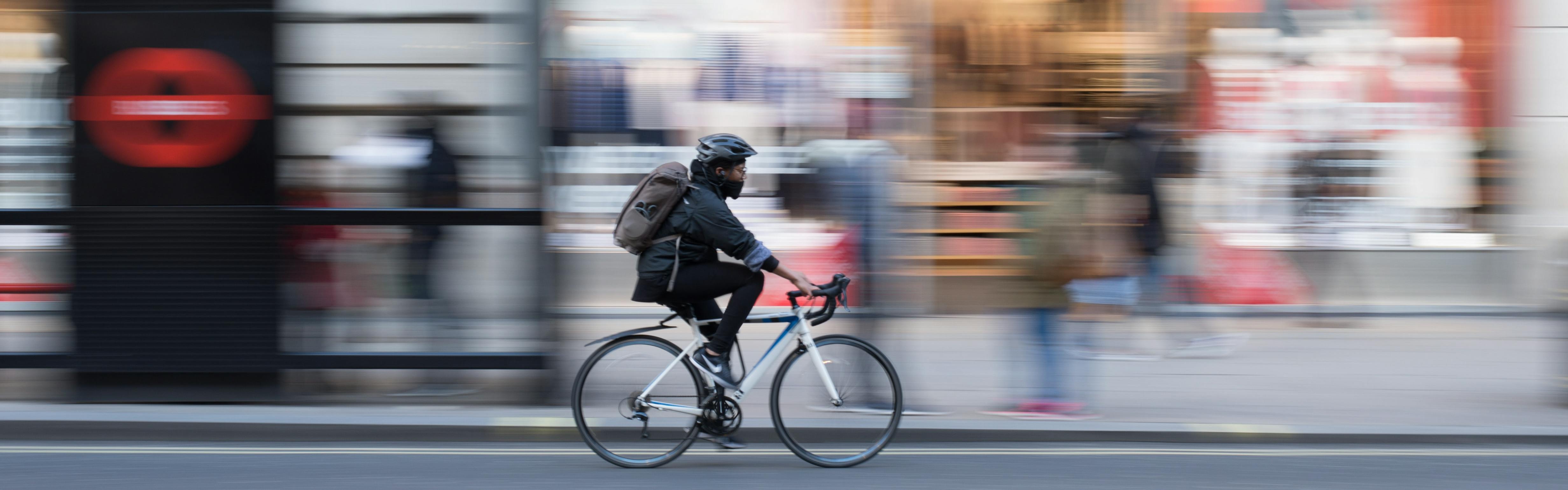 The image is focused on a biker in the middle of the frame. The city scene behind him is blurred. 