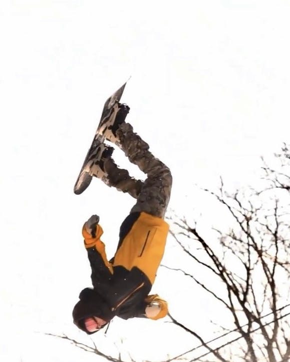A man doing a backflip on the GNU Riders Choice Snowboard.