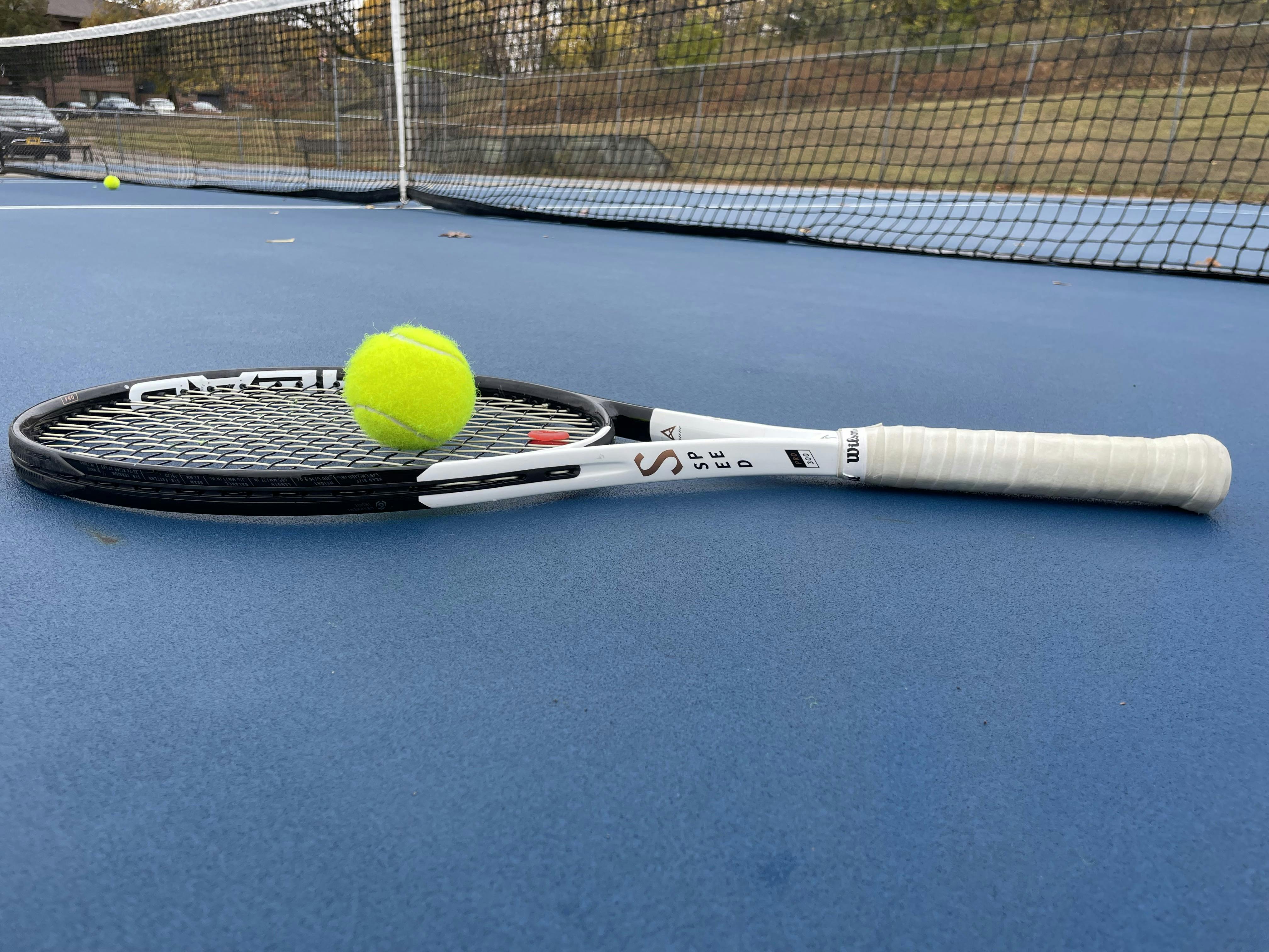 The Head Speed Pro 100 2022 Racquet lying on a tennis court with a tennis ball on it. 