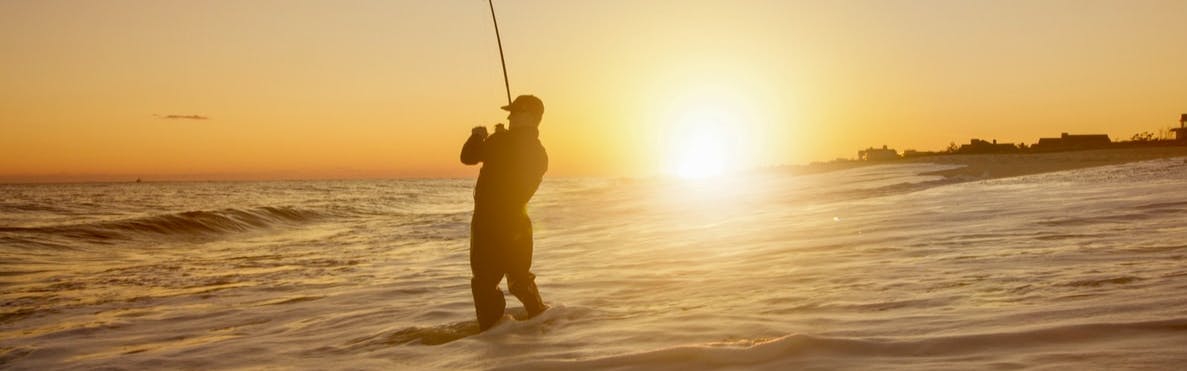 A fisherman fishing in the ocean waves at sunset