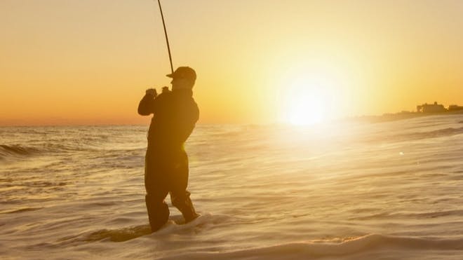 A fisherman fishing in the ocean waves at sunset