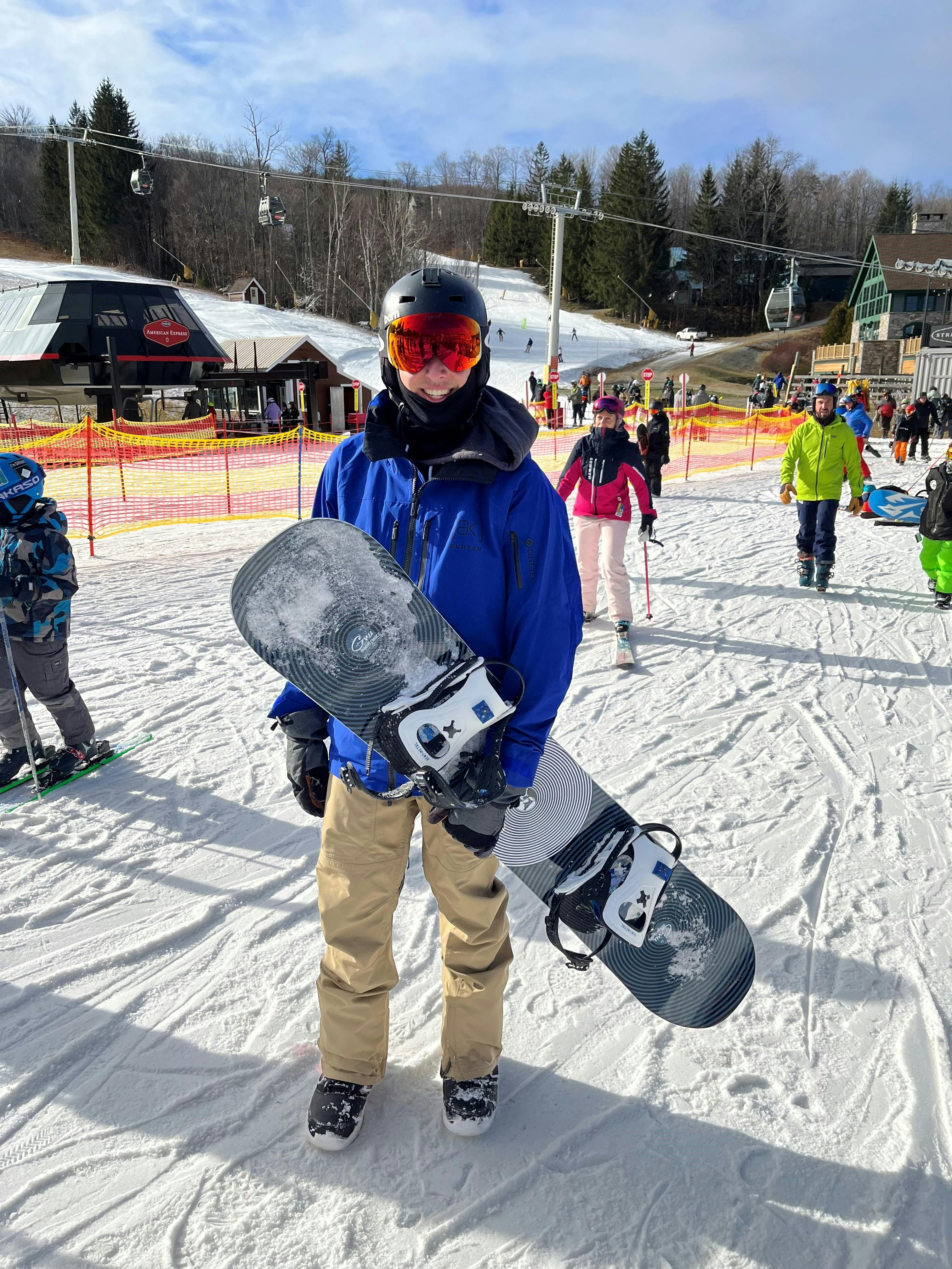 A snowboarder holding his snowboard and wearing the  Burton Men's [ak] Swash GORE‑TEX 2L Jacket.