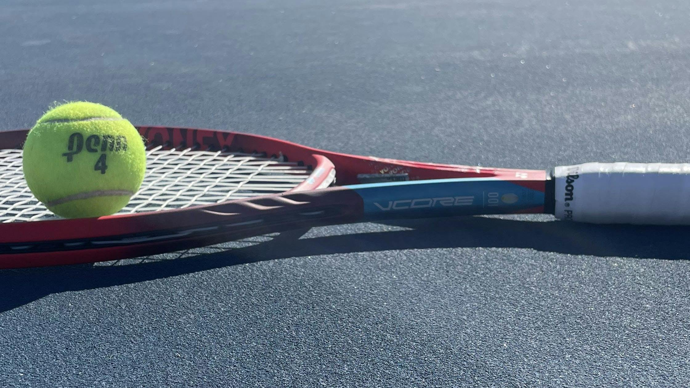The Yonex Vcore 100 Racquet laying on a tennis court. 