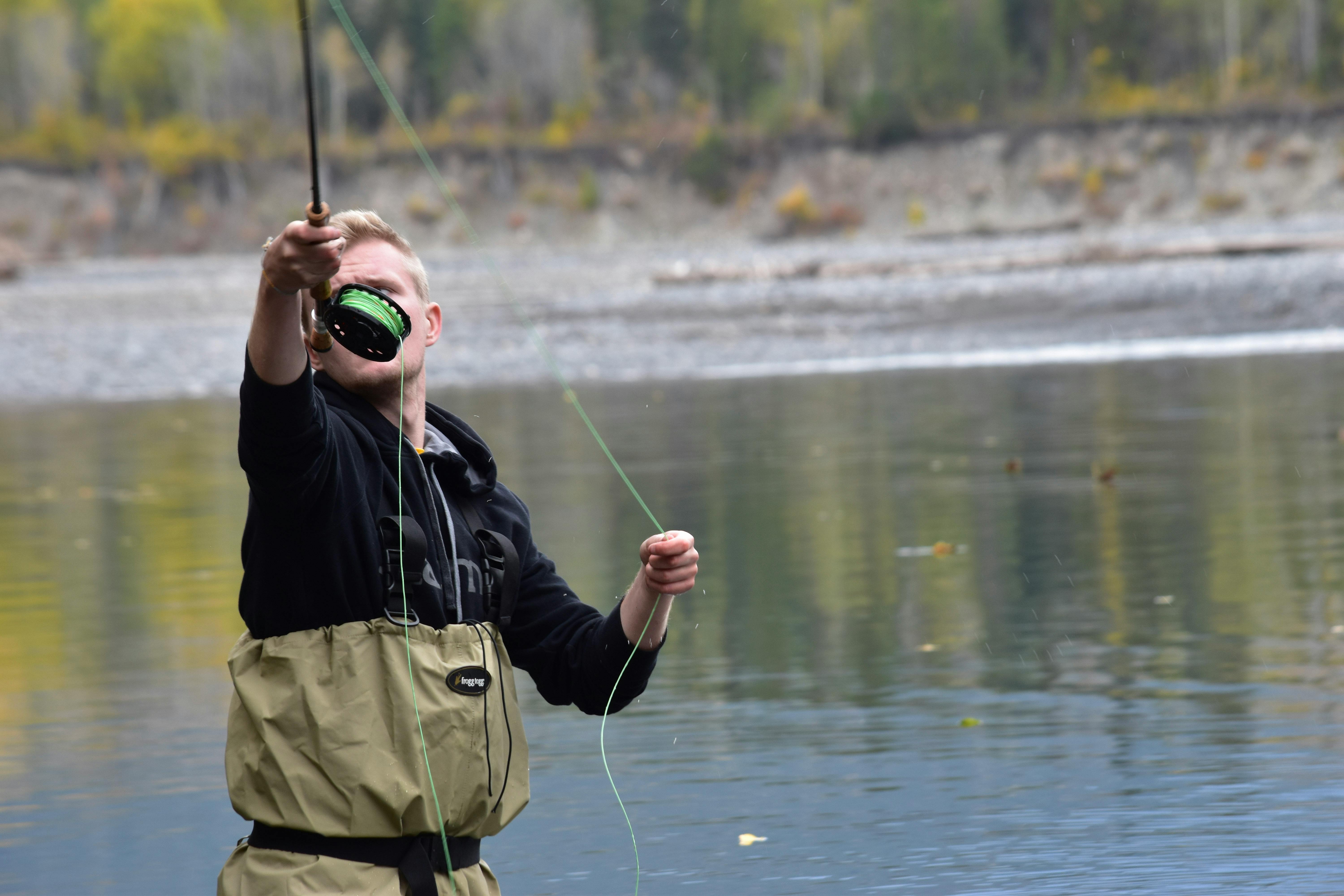A man stands in a river while flyfishing. He extends his arm, holding out the rod. 