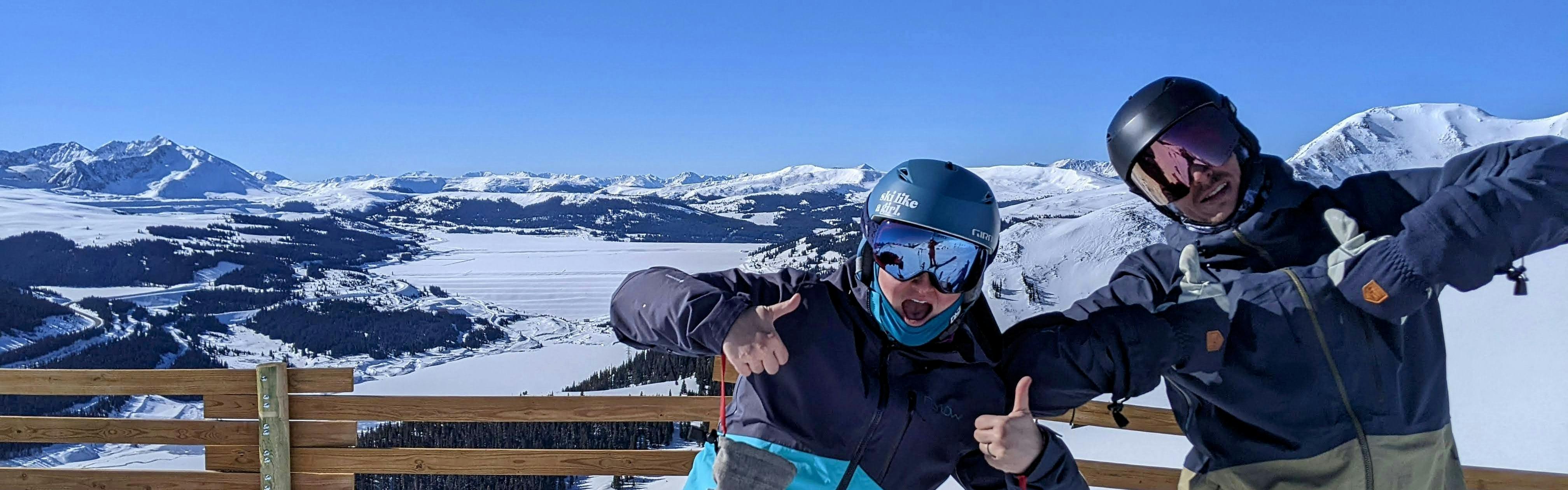 Two skiers at the top of a ski run giving a thumbs up to the camera. 