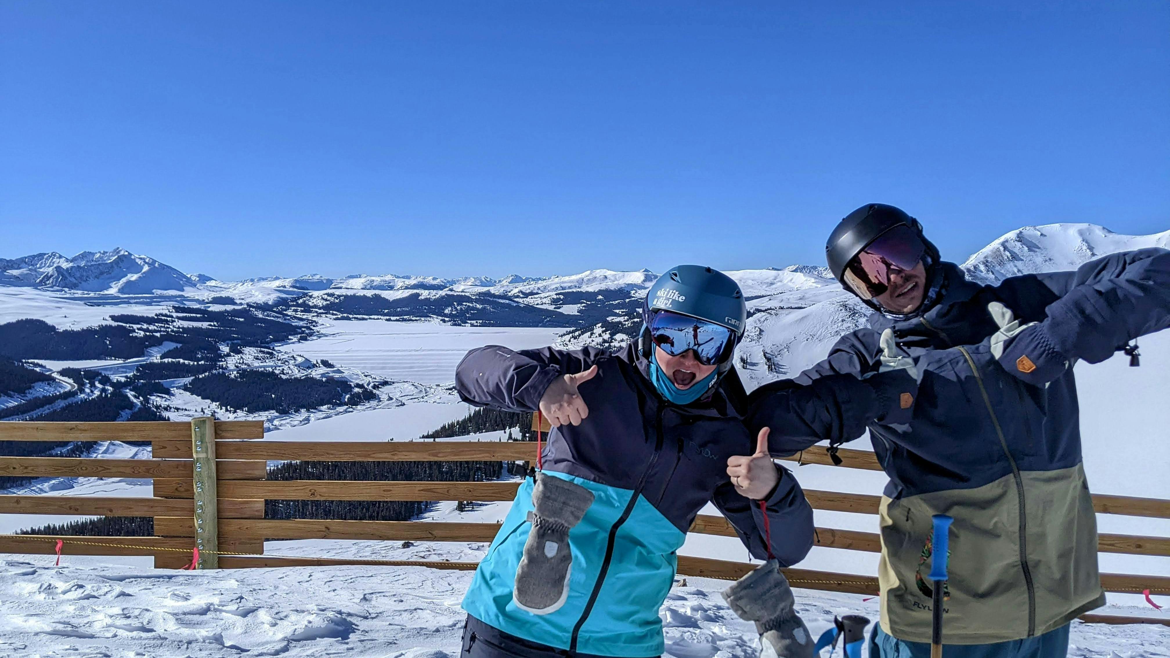 Two skiers at the top of a ski run giving a thumbs up to the camera. 
