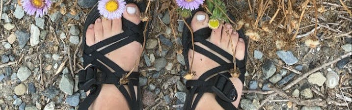 Close up of the chaco sandals on some feet near flowers. 