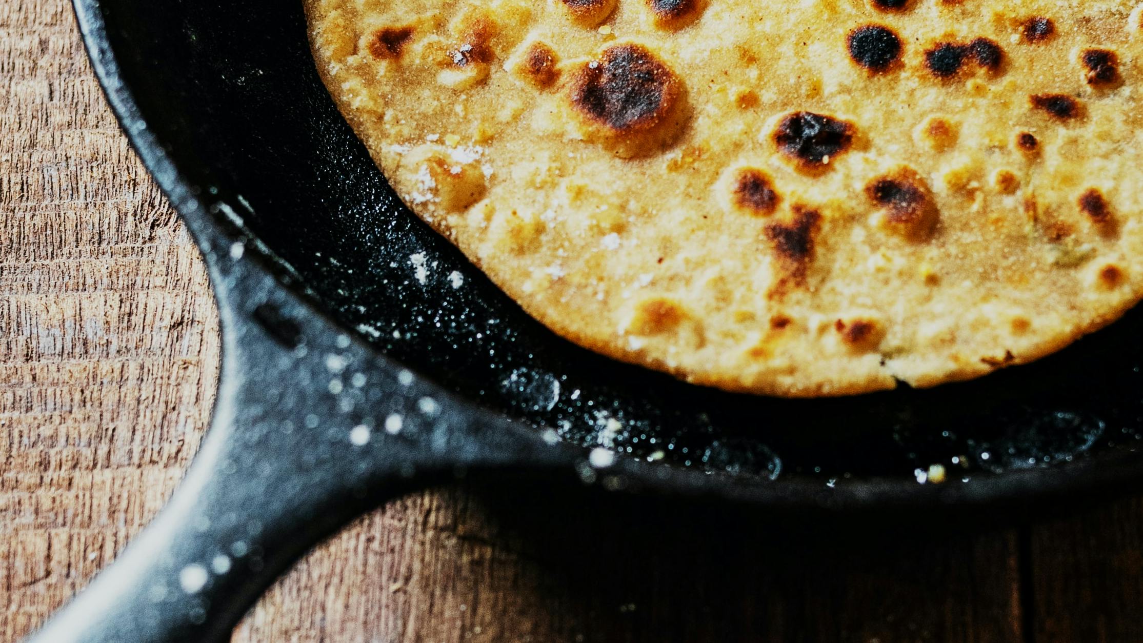 A tortilla sits in a cast-iron skillet that is dusted in flour. 
