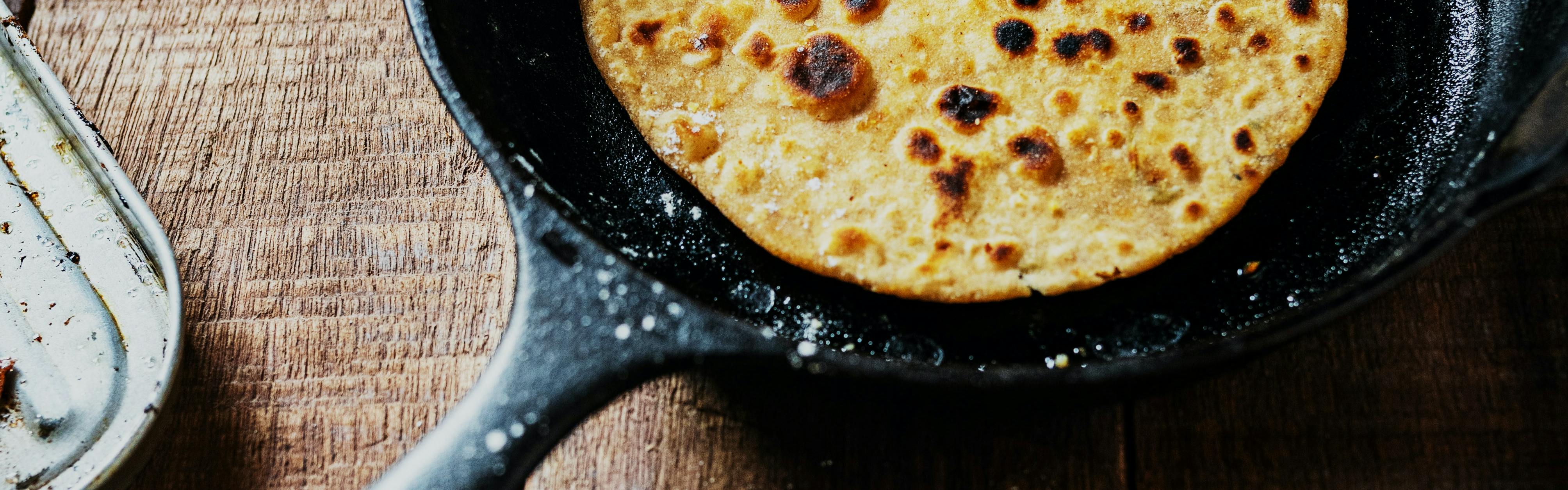 A tortilla sits in a cast-iron skillet that is dusted in flour. 