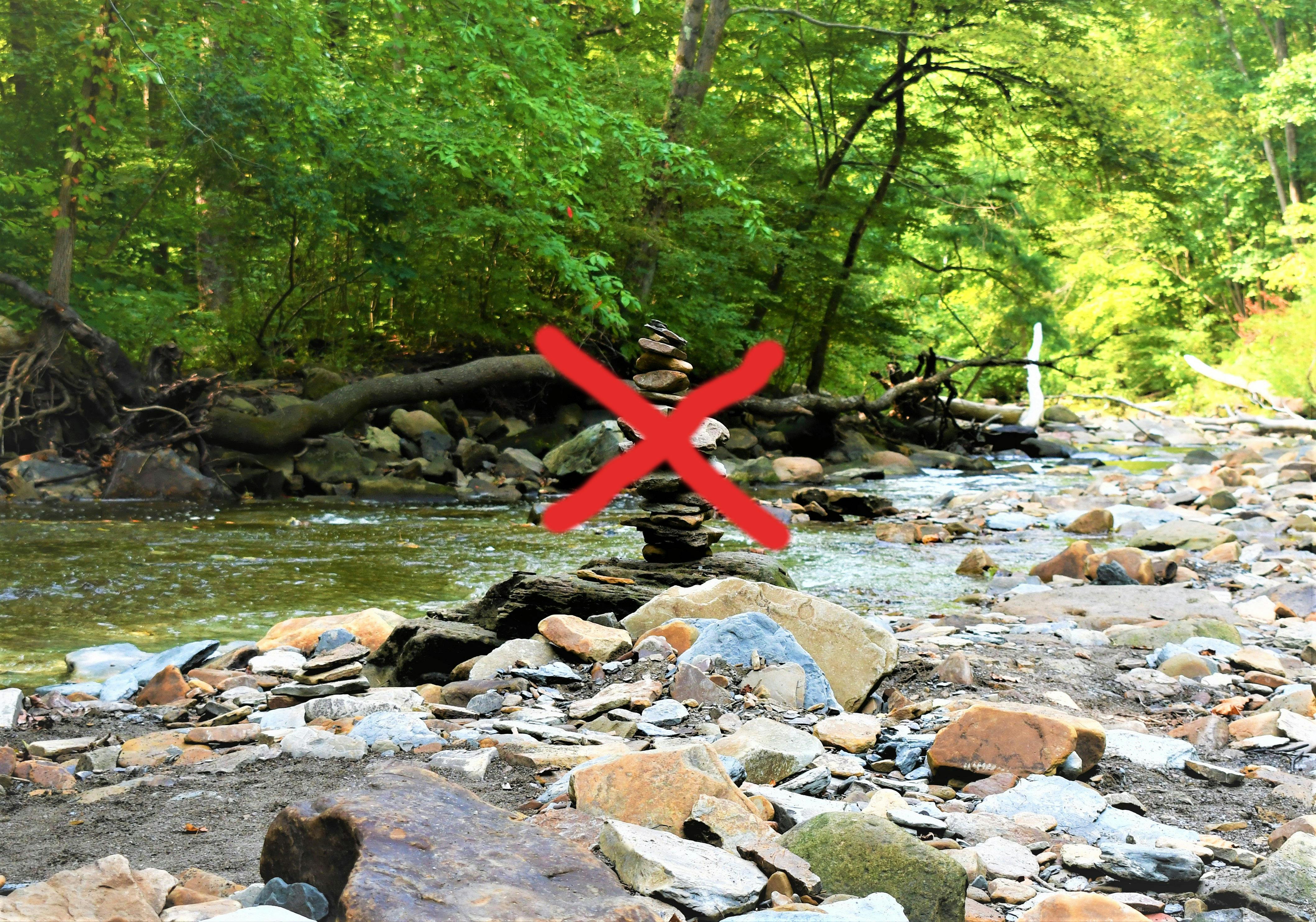 An image of a creekside cairn has been edited with a hand-drawn red X over the cairn--indicating the author's stance on Leave No Trace Principles. 