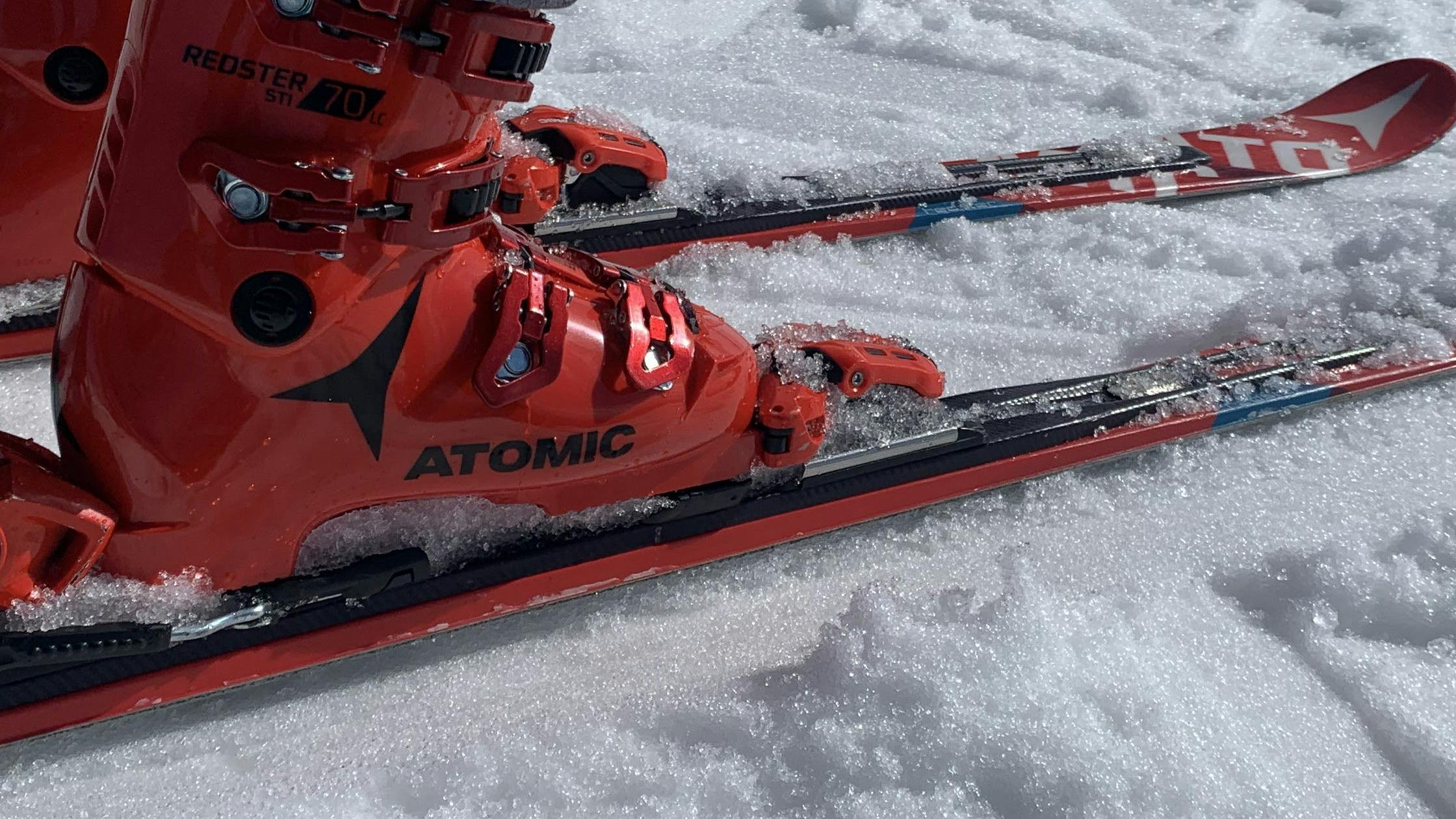 Close up of a pair of Atomic Redster boots and a pair of race skis. There is snow under the skis. 
