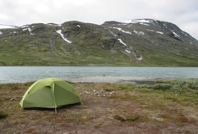 Camping in the high alpine of the Teton Mountain Range. A green tent and a river are visible.