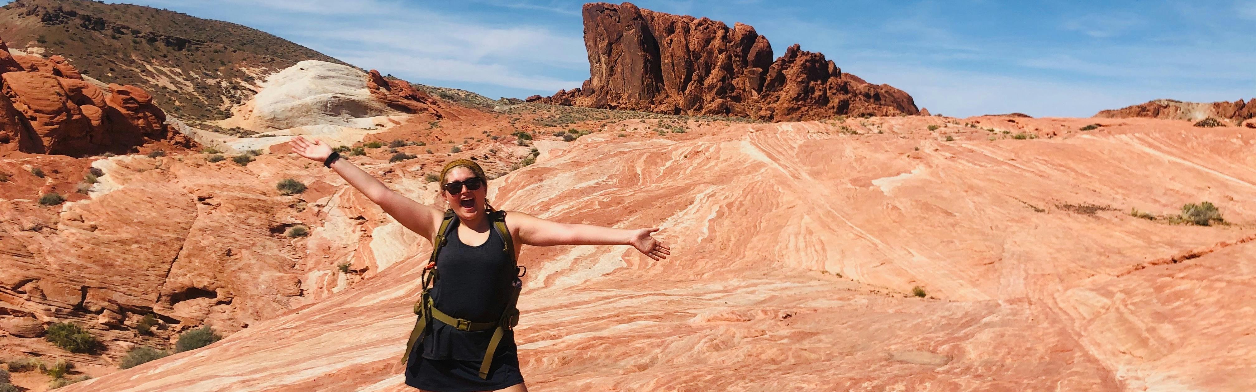The author smiles and holds out her hands in a red rock desert environment. 