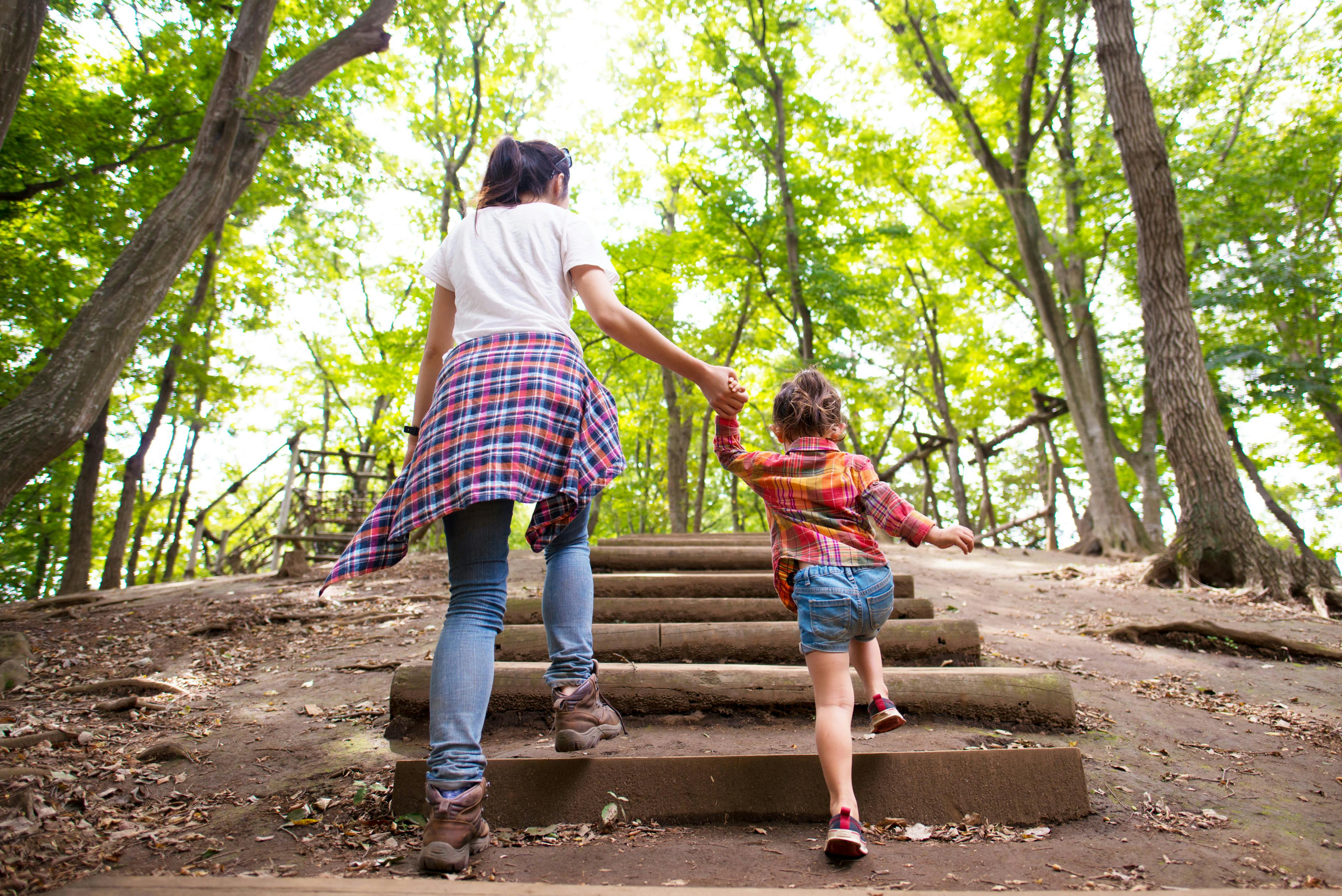 A mom and a daughter climb up wooden steps in a wooded area