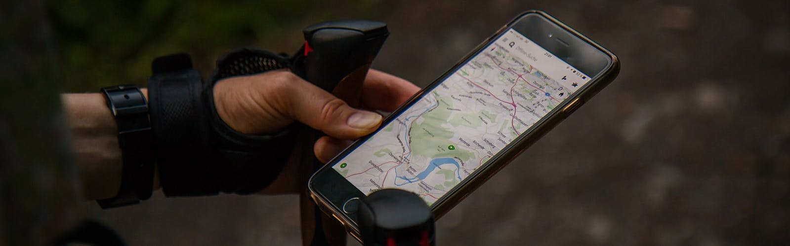 A hiker looks at a map on his phone. He has a hiking pole in his hand as well.