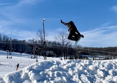 A snowboarder doing a jump and grabbing his board in the air on the Jones Mountain Twin Snowboard.