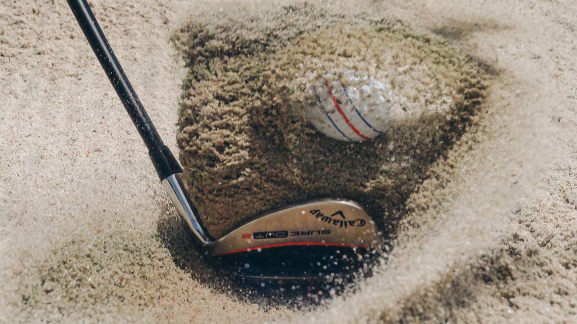 Closeup on a club hitting the ball out of a bunker and sand flying up from contact with the ground
