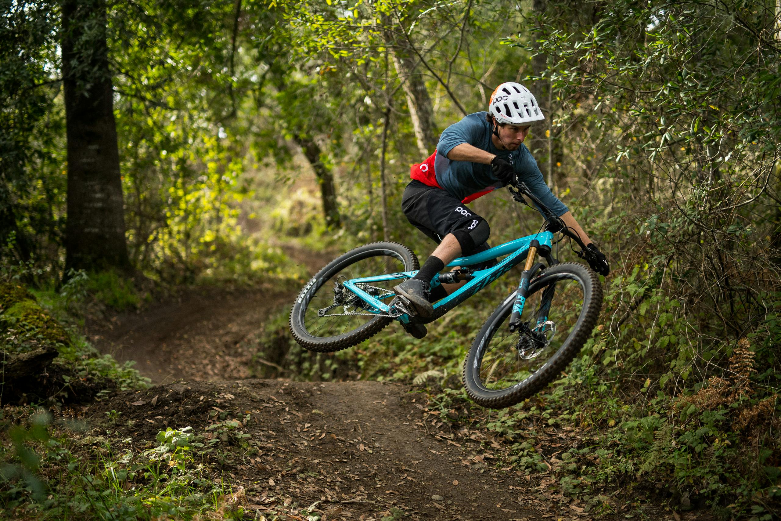 Man on a turquoise mountain bike rounding a bend in the dirt forest path.