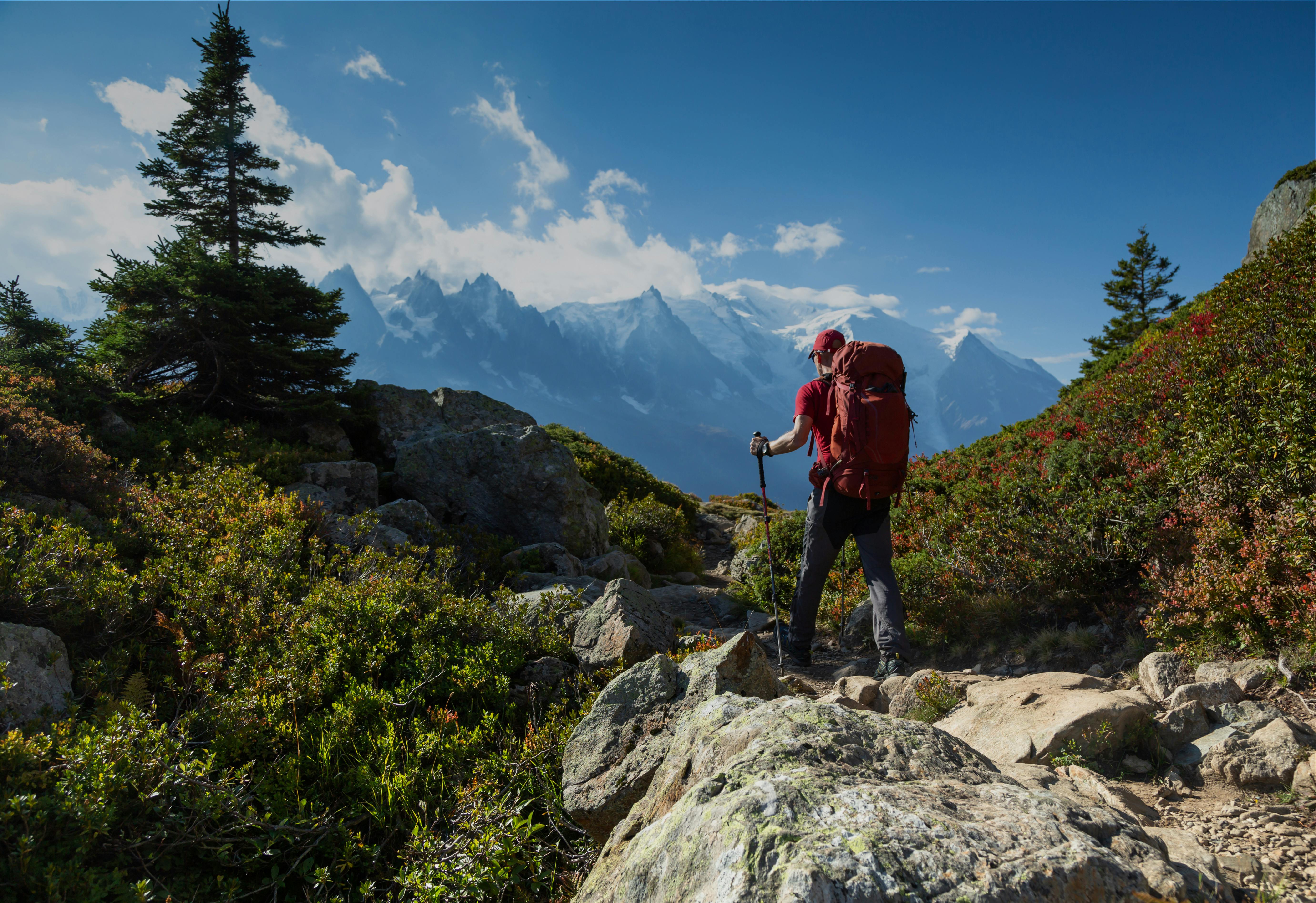 A guy is shown hiking up a rocky hill with hiking poles and a backpack through the mountains