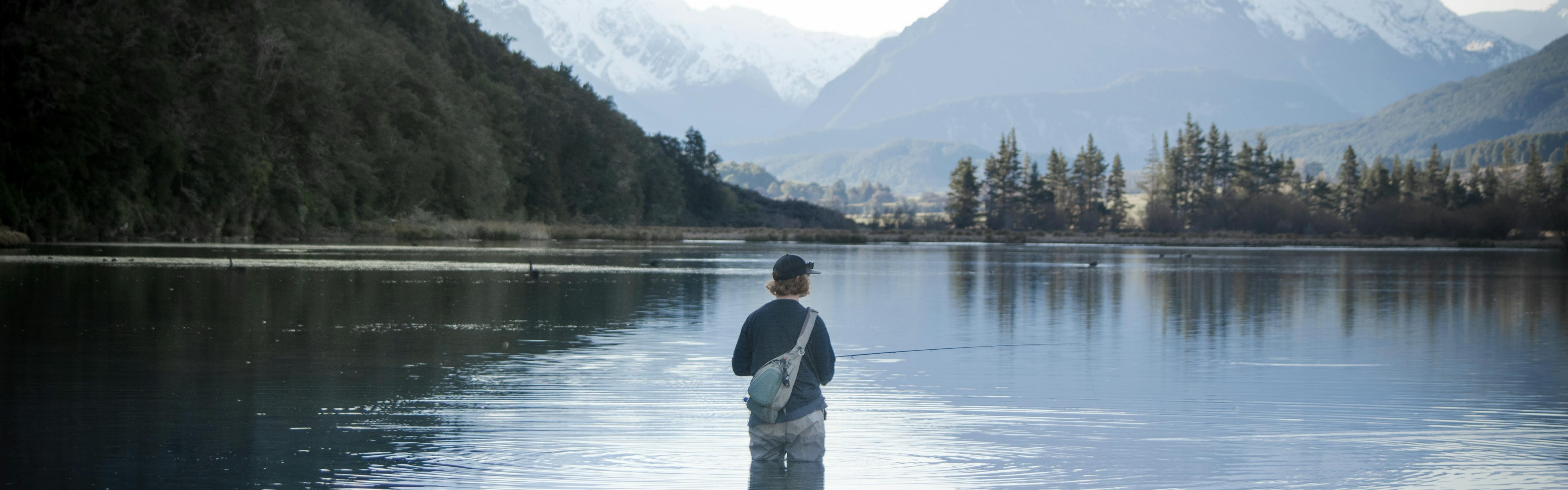 Person stands in the middle of an alpine lake fly fishing.