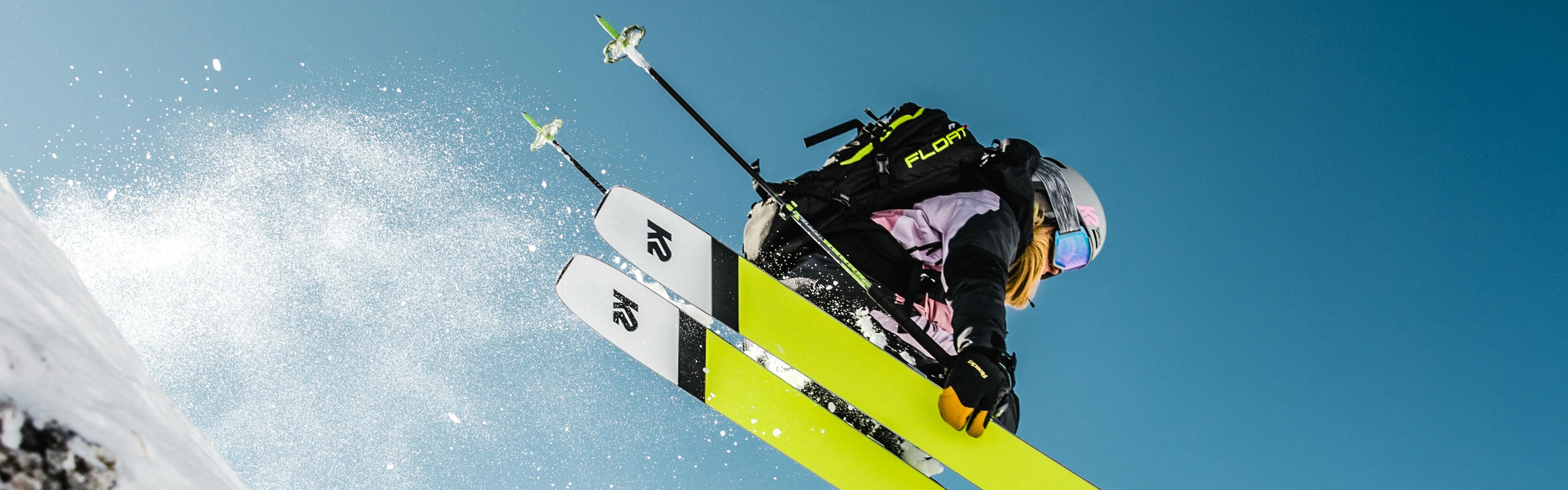 Someone jumps with their green k2 skis. Their poles are pointed behind them. 