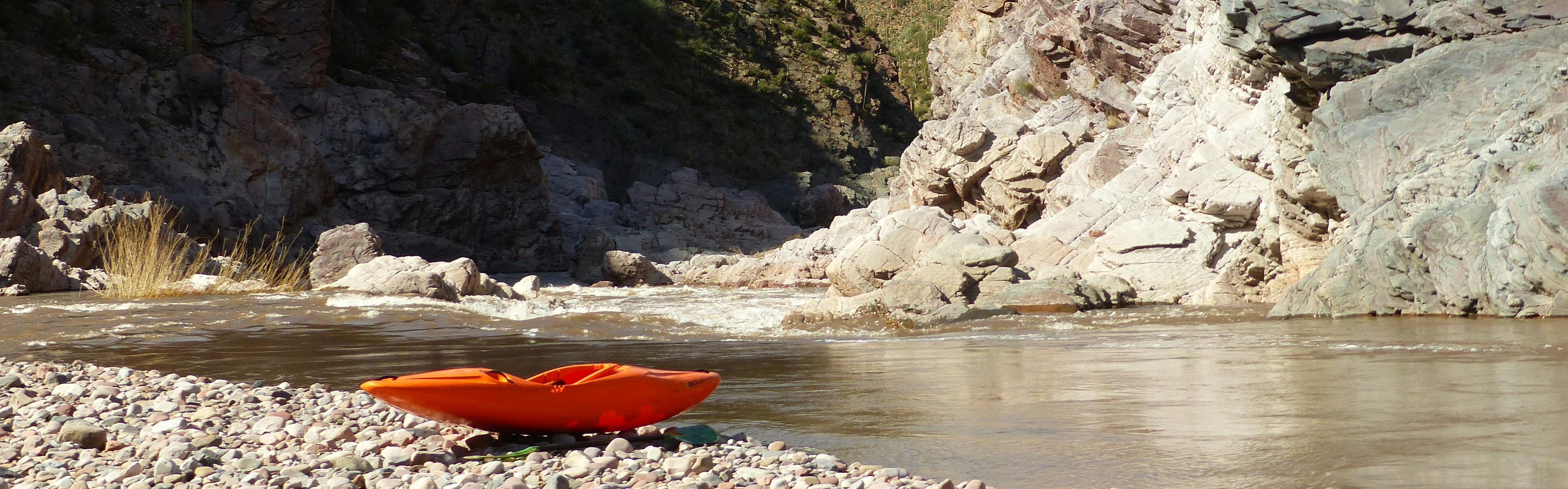 Orange kayak sits on the bank of a river.