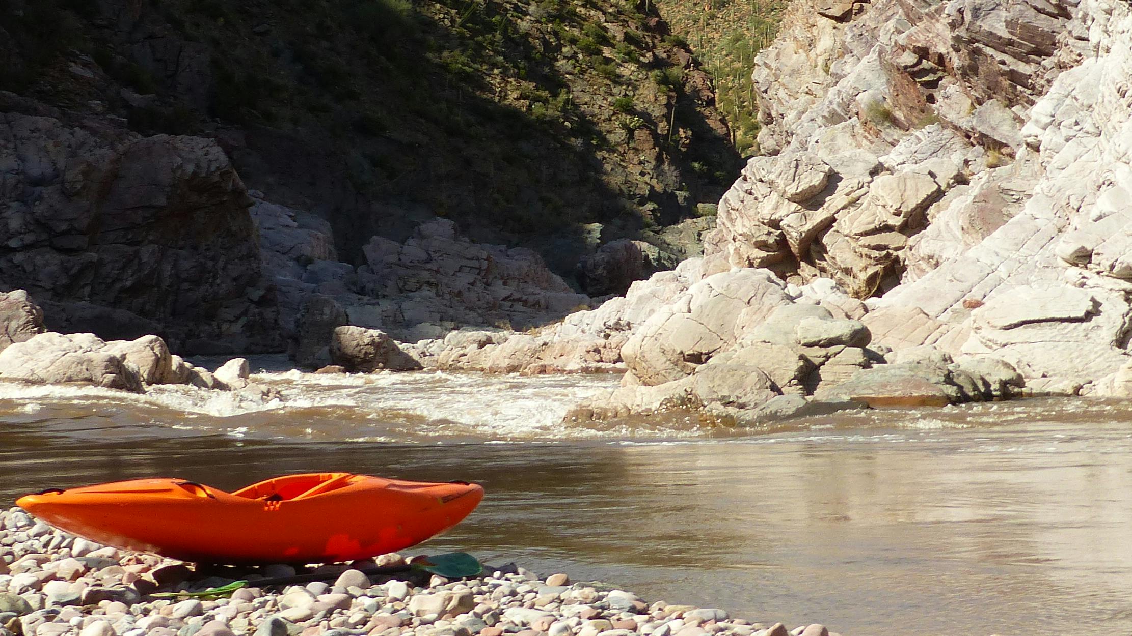 Orange kayak sits on the bank of a river.