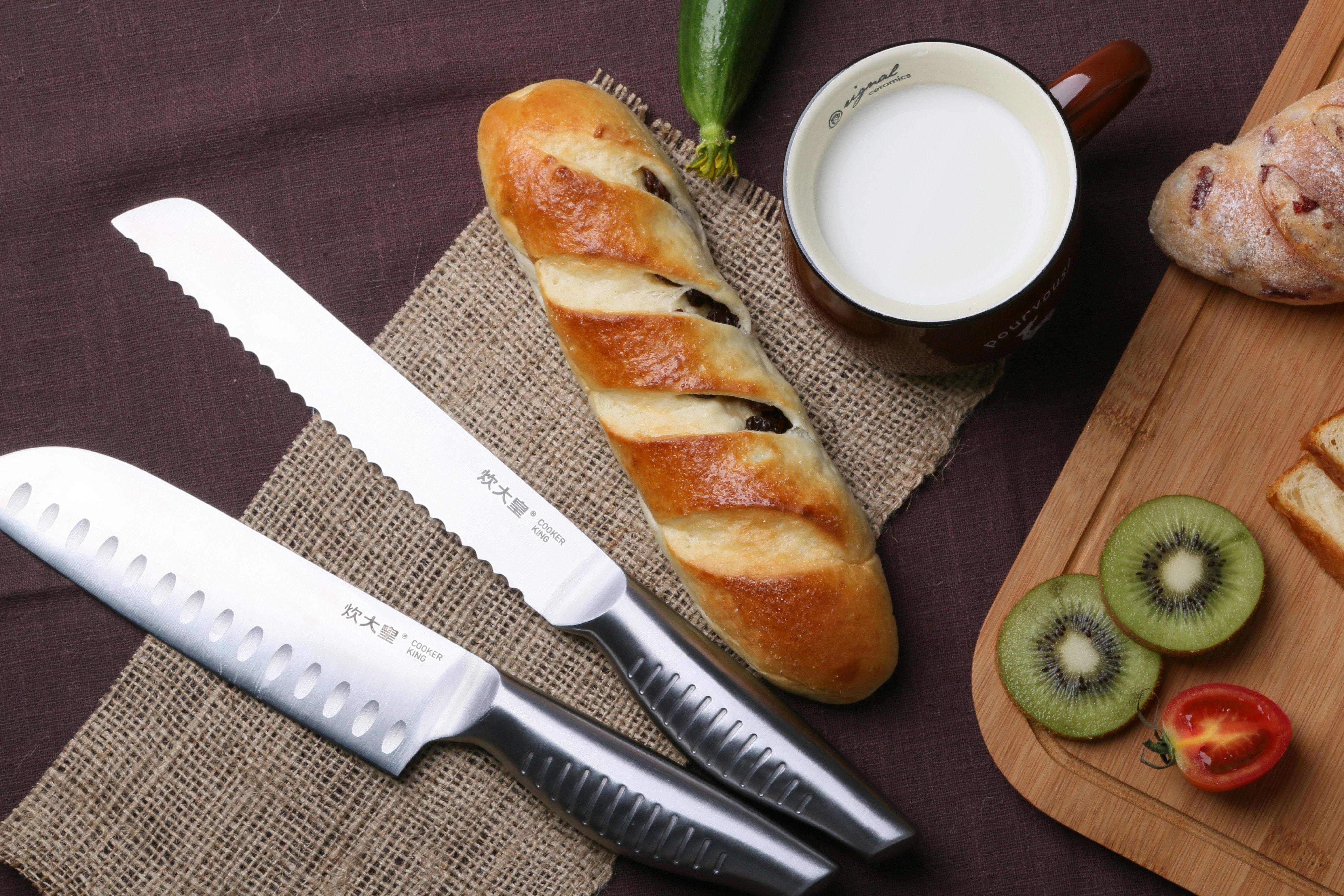 Two knives lay next to some bread and fruit. 