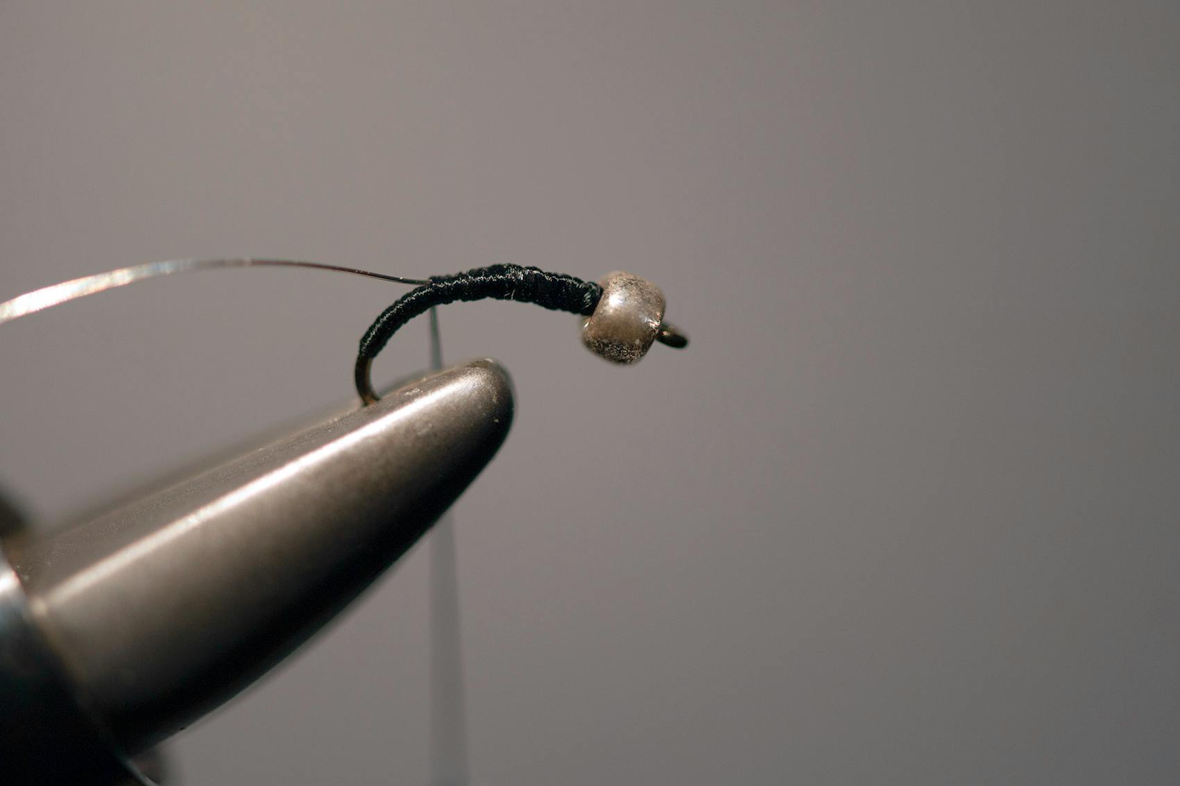 The same hook and bead from above are pictured in the vice jaws with more thread around the hook.