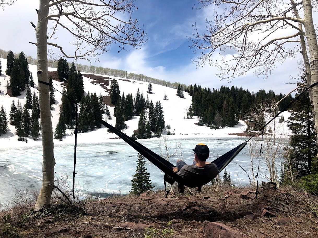 A man sits in a hammock with a lake in the background. 