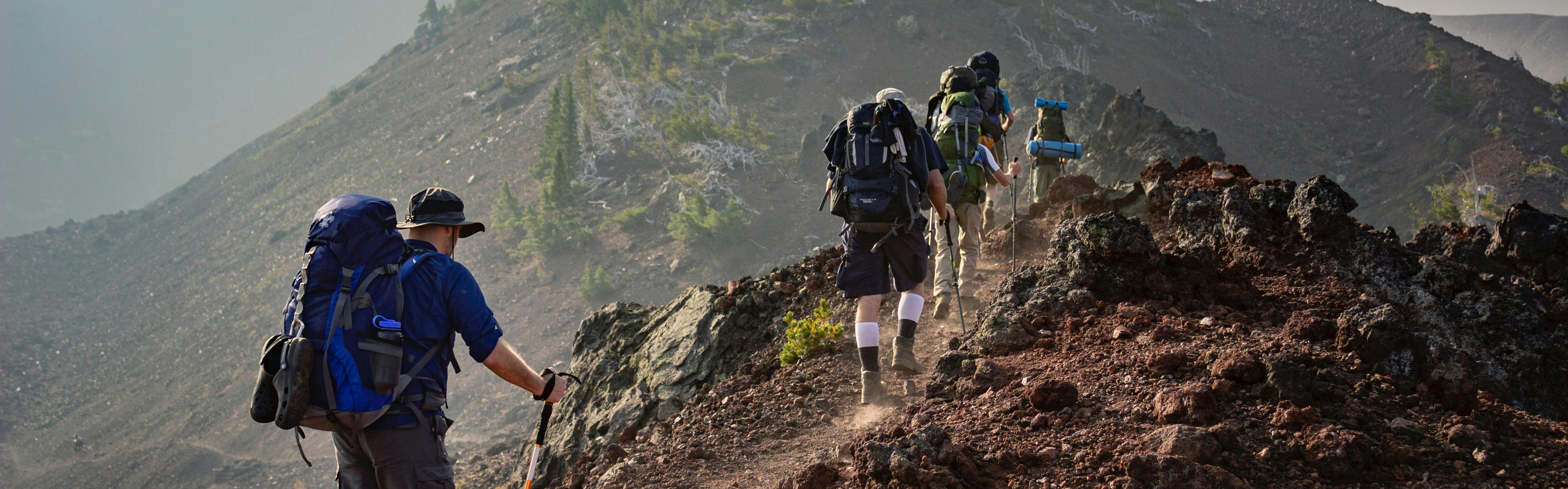 People with large backpacks hike along a dusty ridge