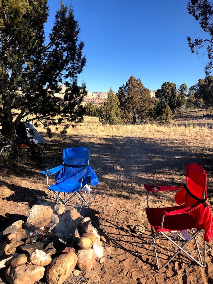 A red folding chair and a blue folding chair sitting around a campfire.