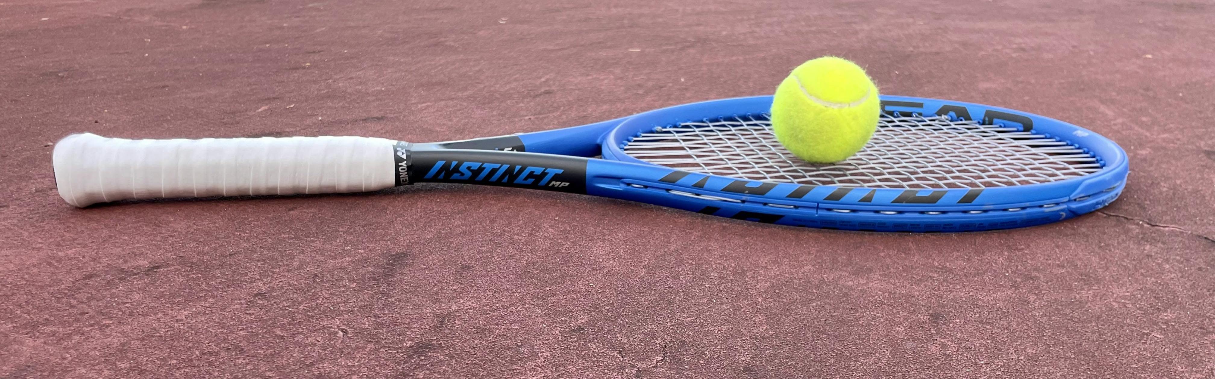 A Head Instinct MP 2022 Racquet lying on a tennis court. 