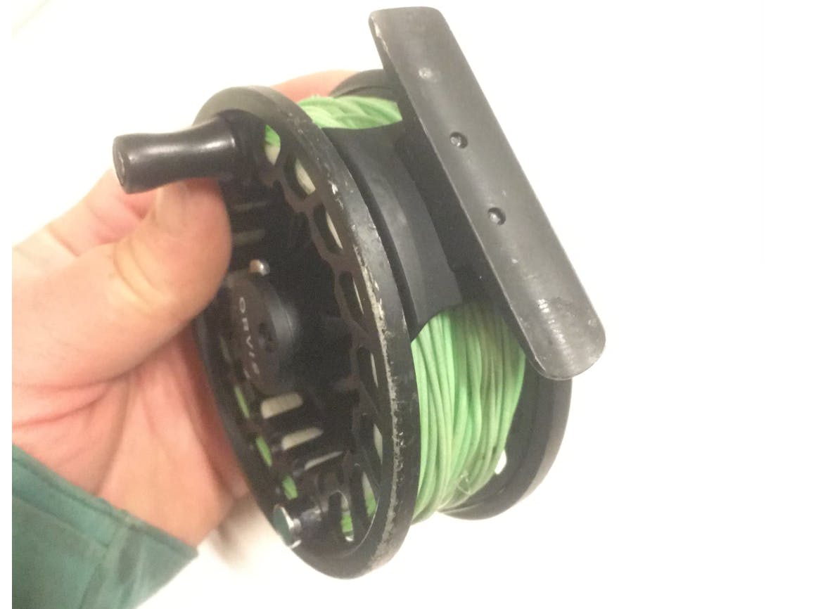 A hand holding the Orvis Clearwater LA Reel. 