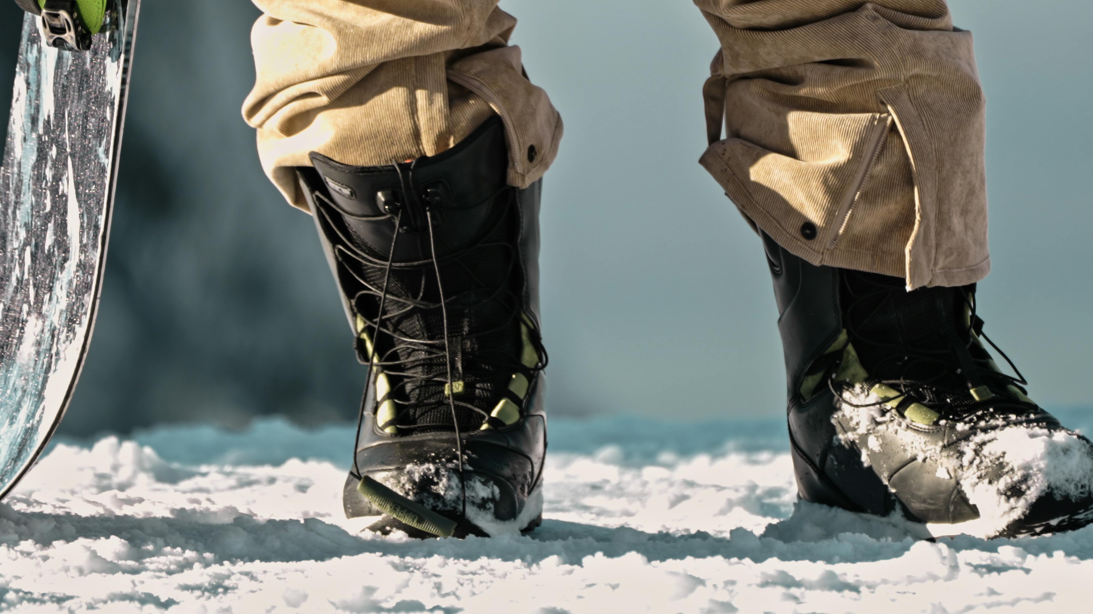 Close up of snowboard boots as a snowboarder is wearing them while holding his snowboard.