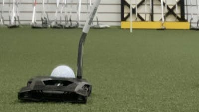 The Cobra King 3D Printed Agera Putter in front of a ball at a golf club store. 