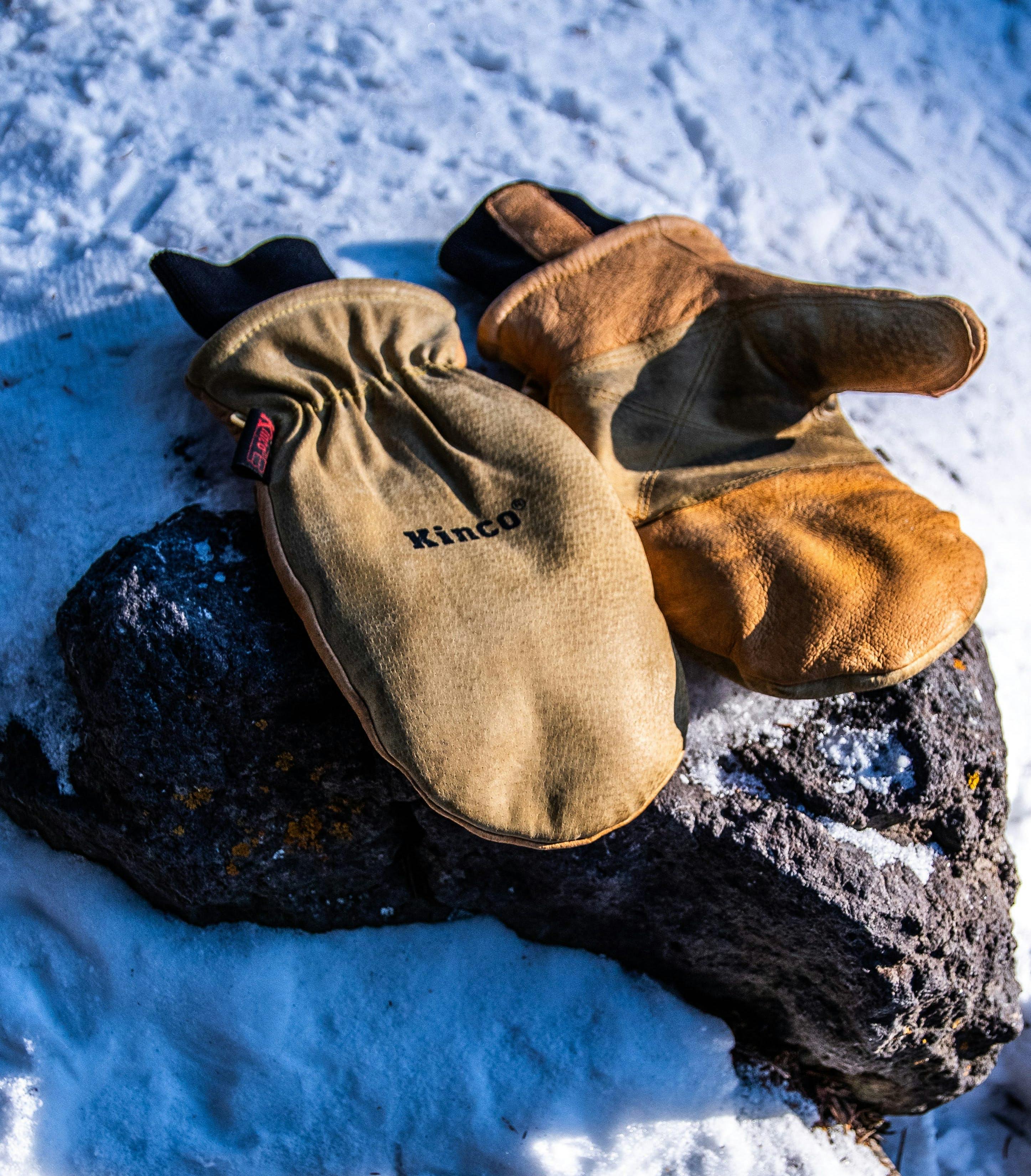 A pair of leather mittens sit on a rock in the snow.