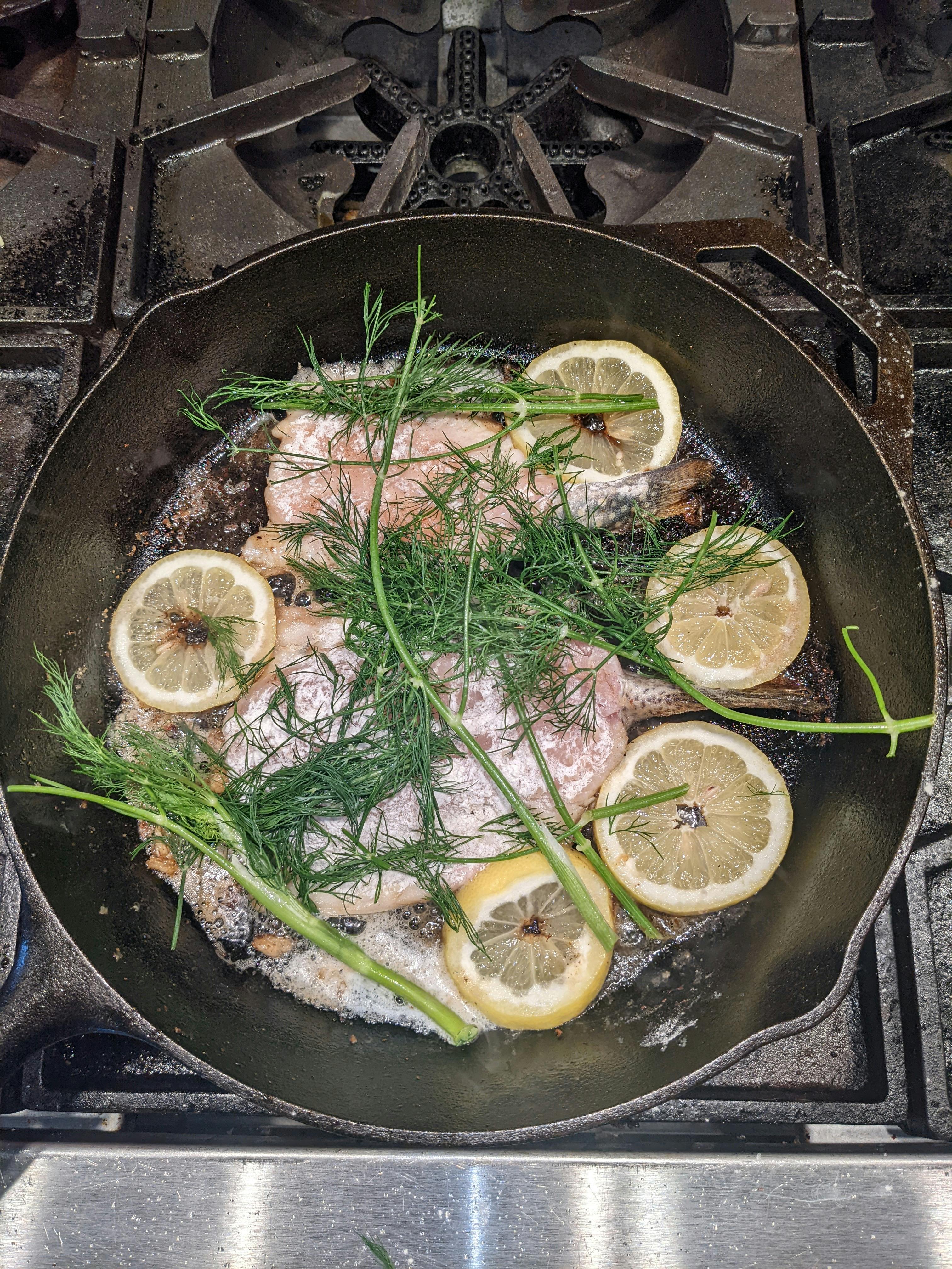 A fish sits in a pan with herbs and lemon.